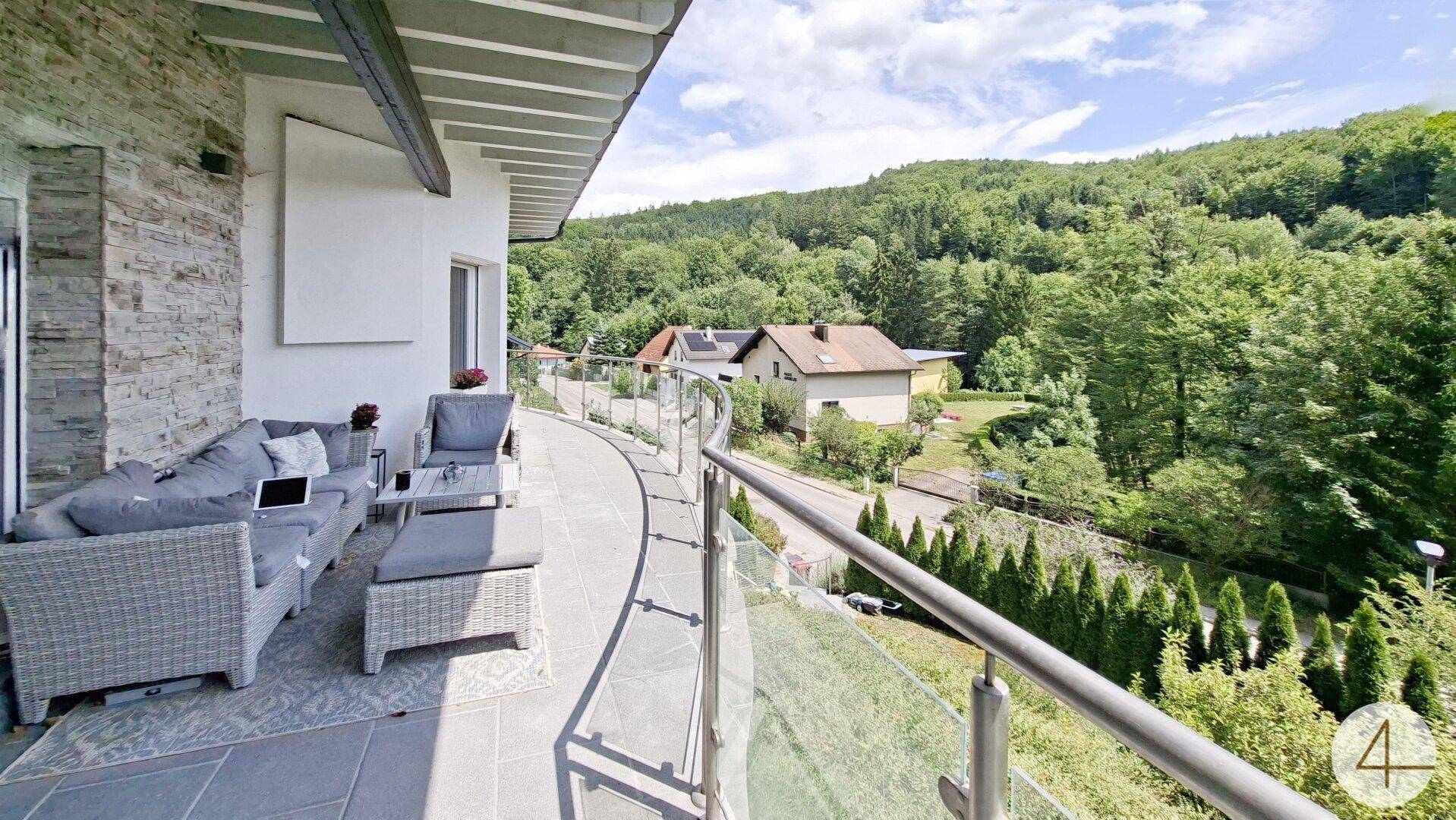 Langer Balkon mit bequemen Outdoor-Möbeln und weitem Blick auf die grüne Landschaft.