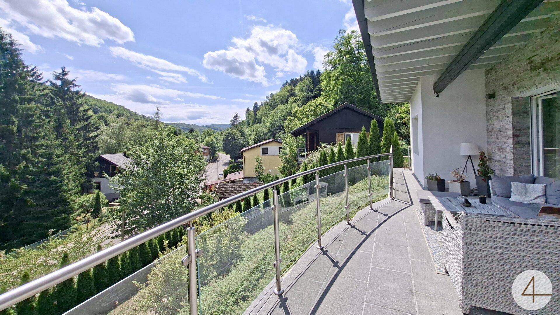 Geräumiger Balkon mit Glasgeländer und Panoramablick auf die umliegende Natur und Häuser.