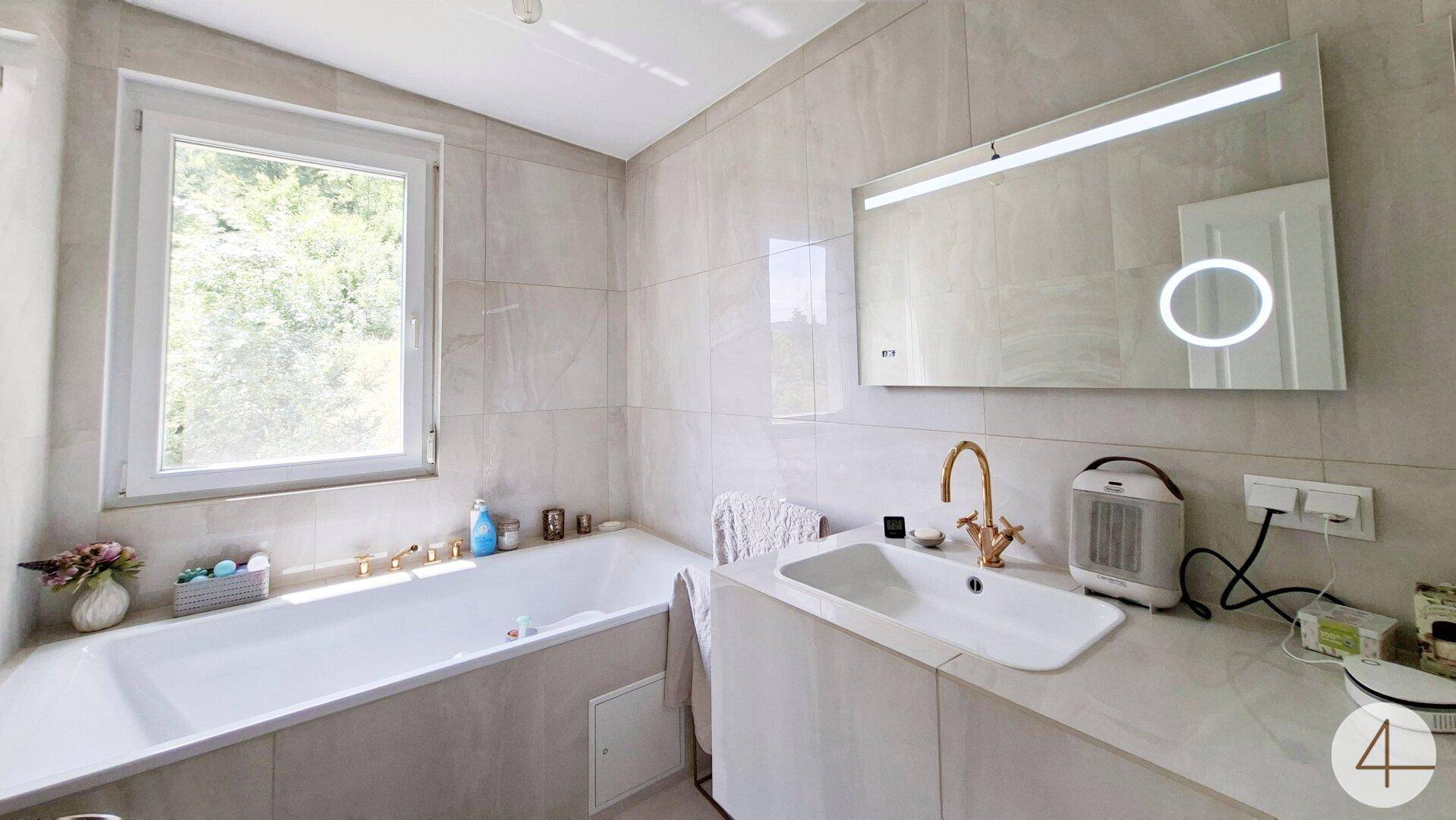 Modernes Badezimmer mit Badewanne, Einzelwaschbecken und beleuchtetem Spiegel.