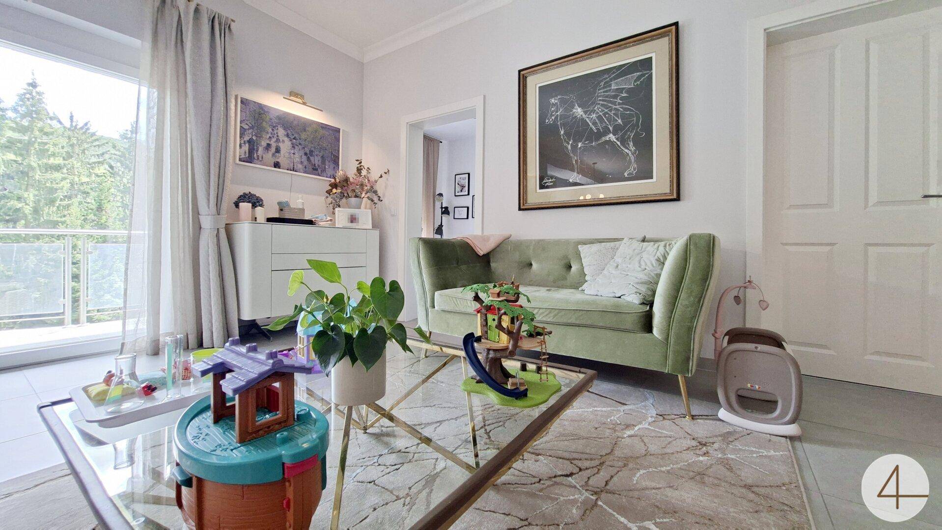 Gemütliches Wohnzimmer mit grünem Sofa, Couchtisch und Zugang zu einem Balkon.