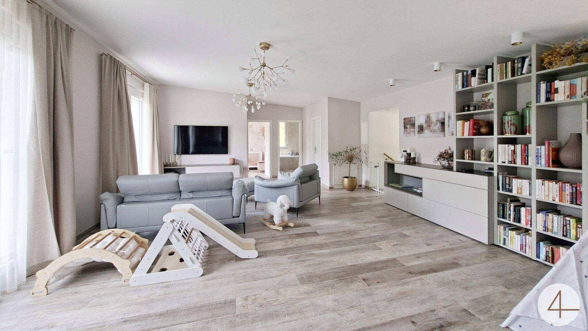 Modern eingerichtetes Wohnzimmer mit Bücherregal, bequemen Sofas und Spielbereich für Kinder.