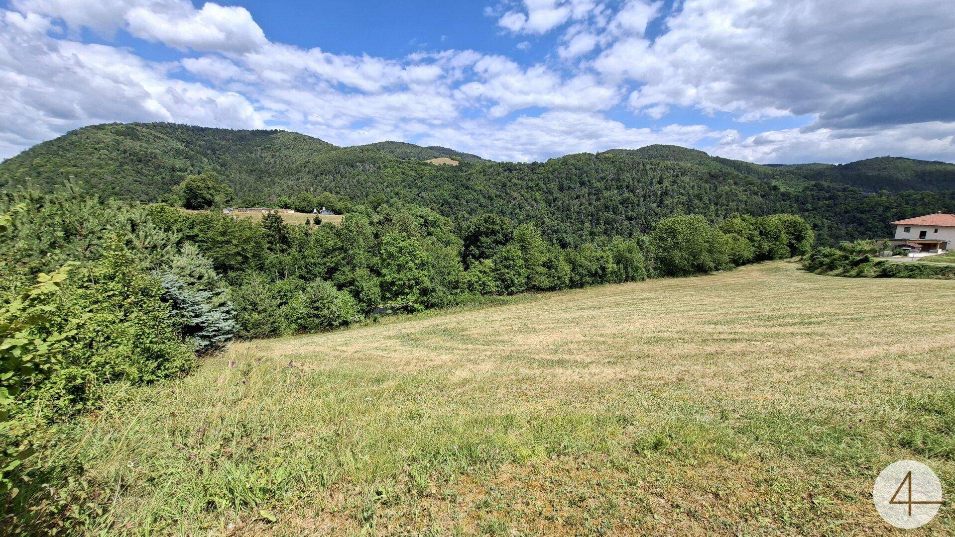 Großes, gemähtes Feld mit weitem Blick auf die bewaldeten Hügel und ein entferntes Haus.