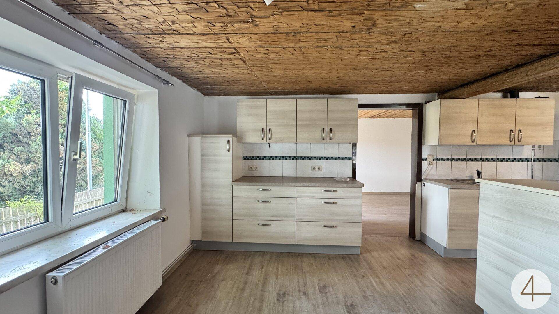 Helle Küche mit Holzbalkendecke, Einbauschränken und großem Fenster mit Blick ins Grüne.