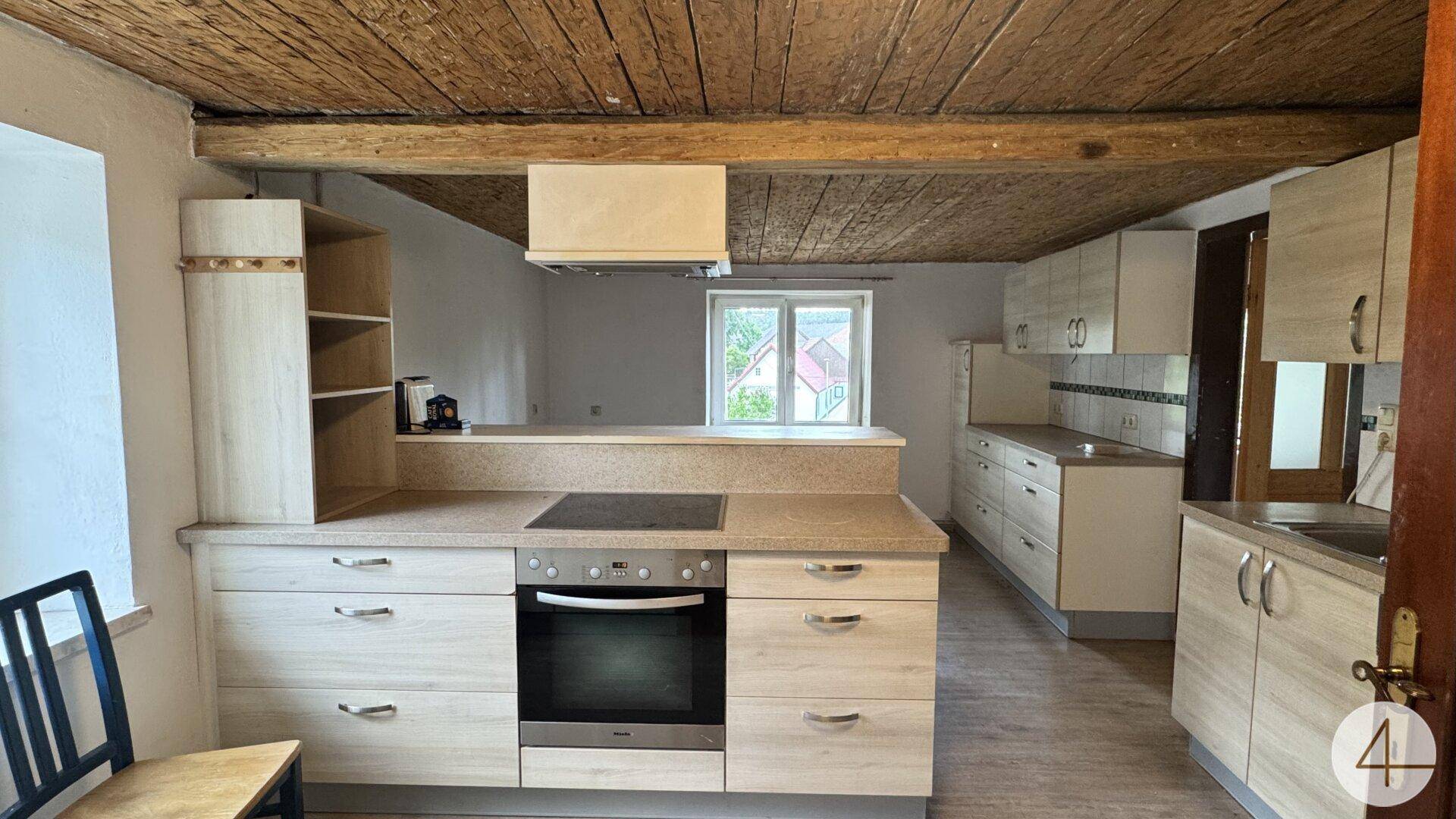 Rustikale Küche mit Holzbalkendecke, Einbauküche und Kochfeld in der Arbeitsplatte.
