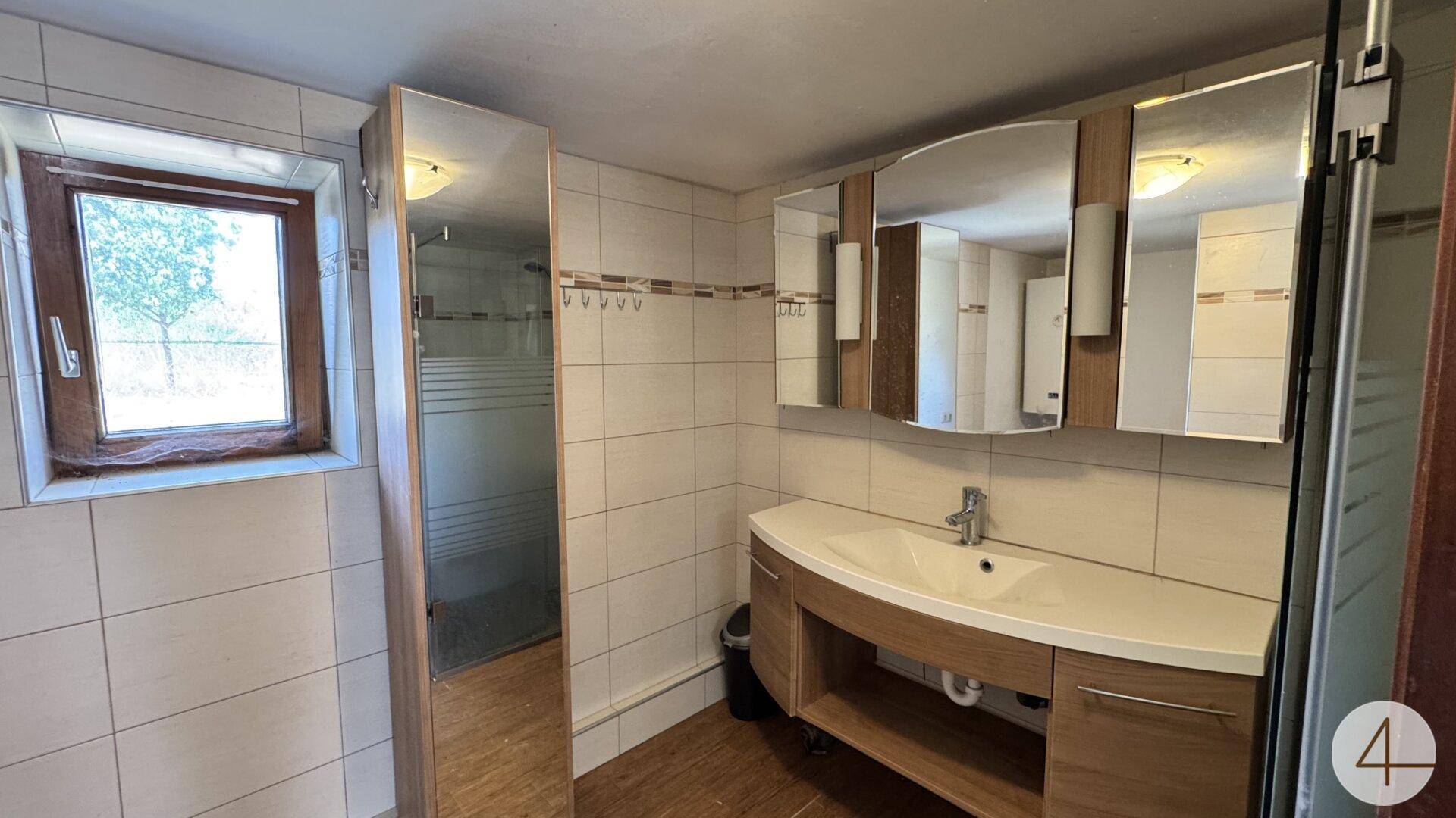 Gefliestes Badezimmer mit Waschtisch, Spiegelschrank und Fenster für Tageslicht.