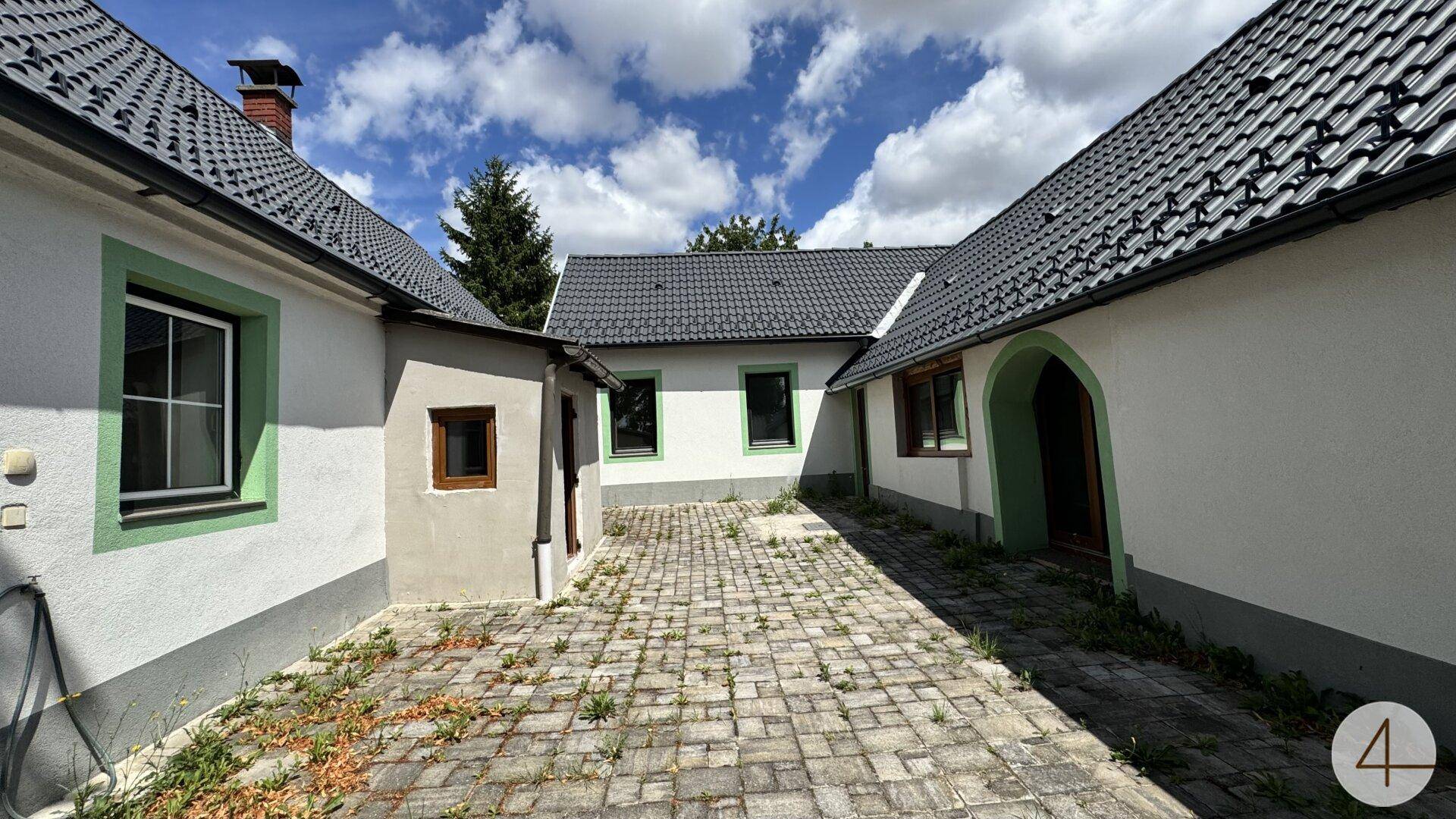 Innenhof mit Pflastersteinen zwischen mehreren Gebäudeteilen unter blauem Himmel.