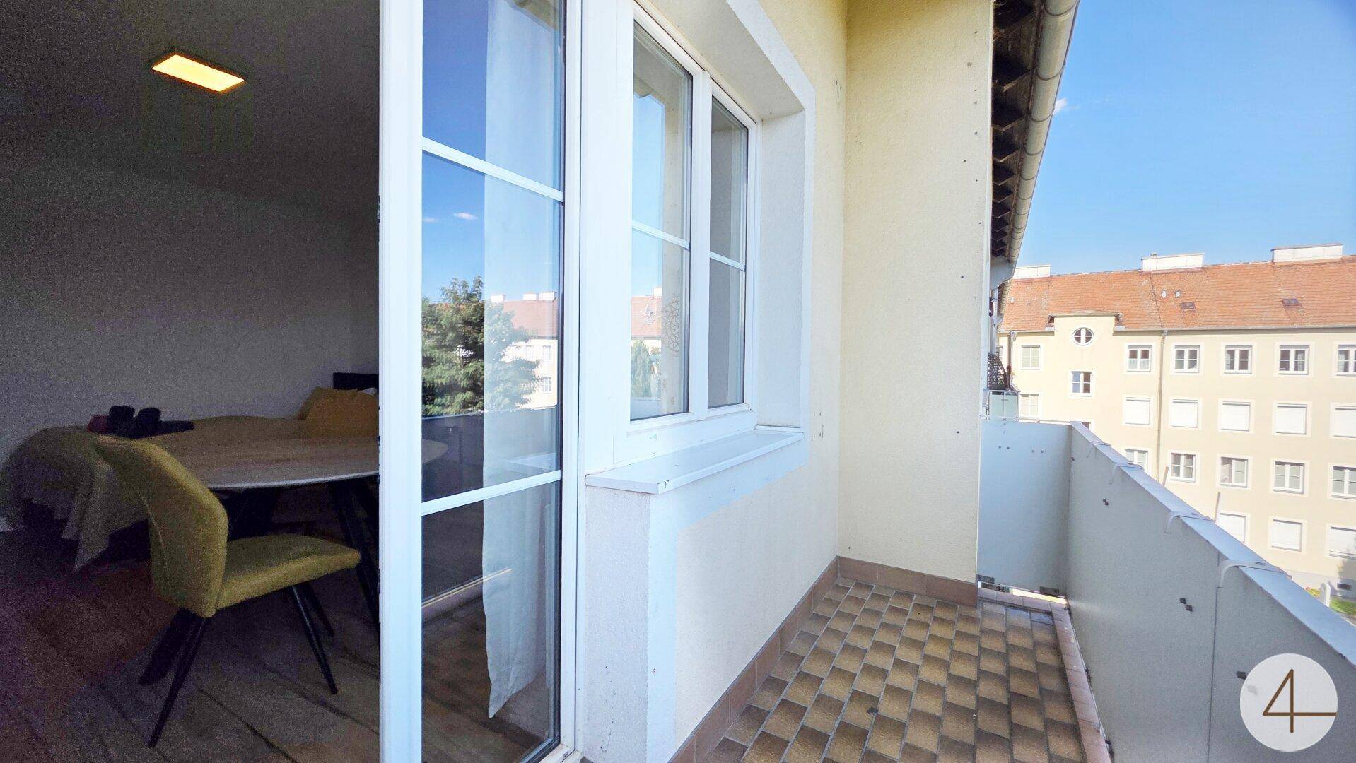 Heller Balkon mit Fliesenboden und Zugang zu einem möblierten Innenraum.