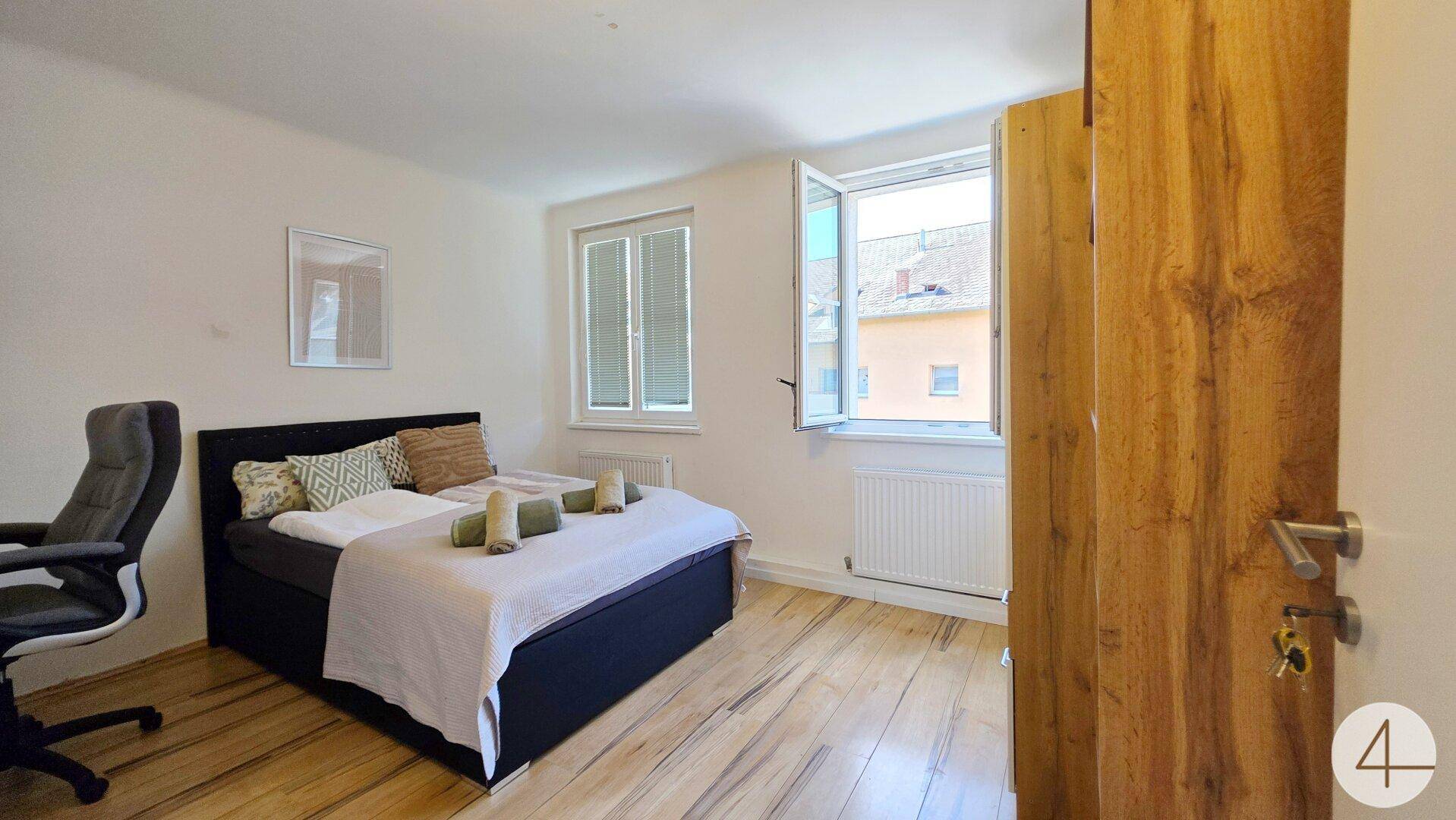 Helles Schlafzimmer mit Holzboden, Doppelbett und zwei Fenstern für viel Tageslicht.
