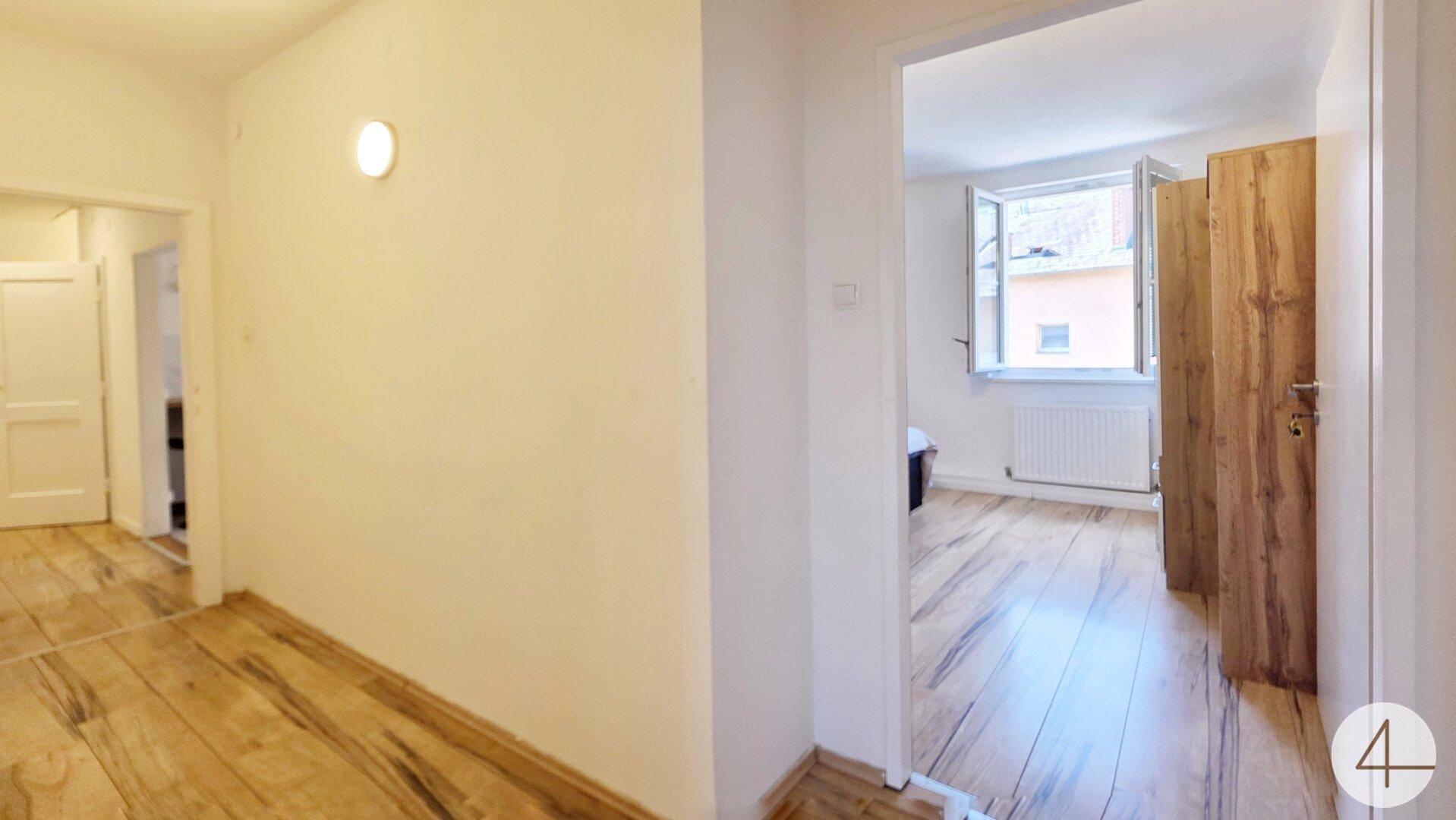 Heller Flur mit Holzboden, der zu einem weiteren Zimmer mit Fenster führt.