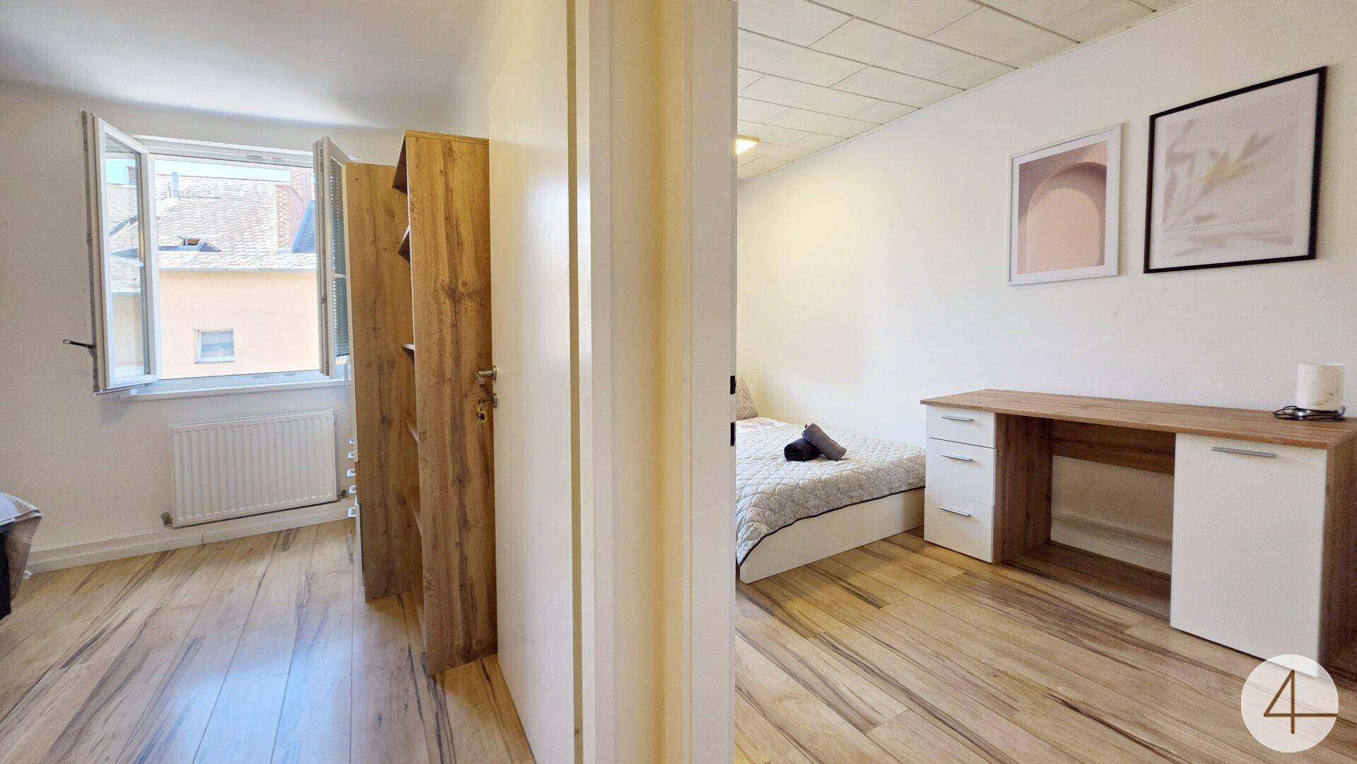 Blick vom Flur in ein helles Schlafzimmer mit Holzboden und Arbeitsbereich.
