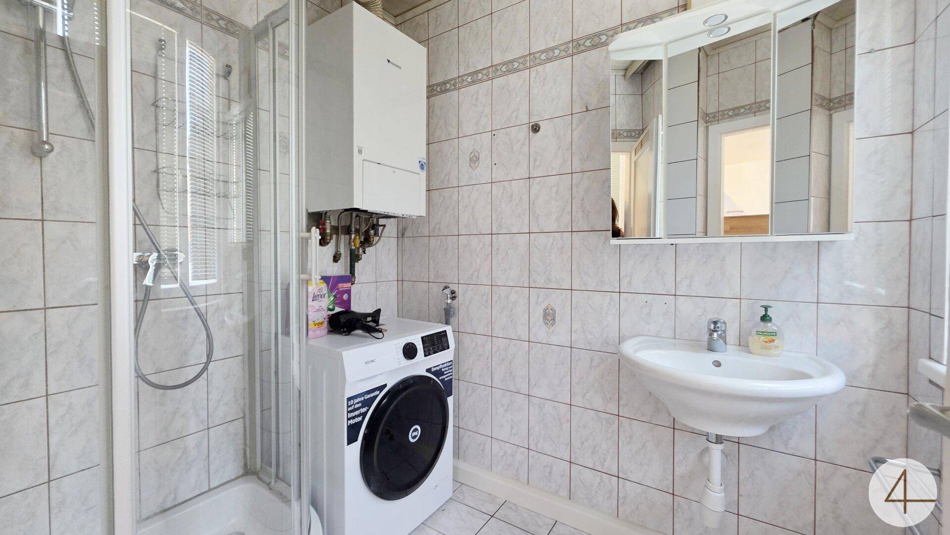 Funktionales Badezimmer mit Dusche, Waschbecken, Waschmaschine und Spiegelschrank.