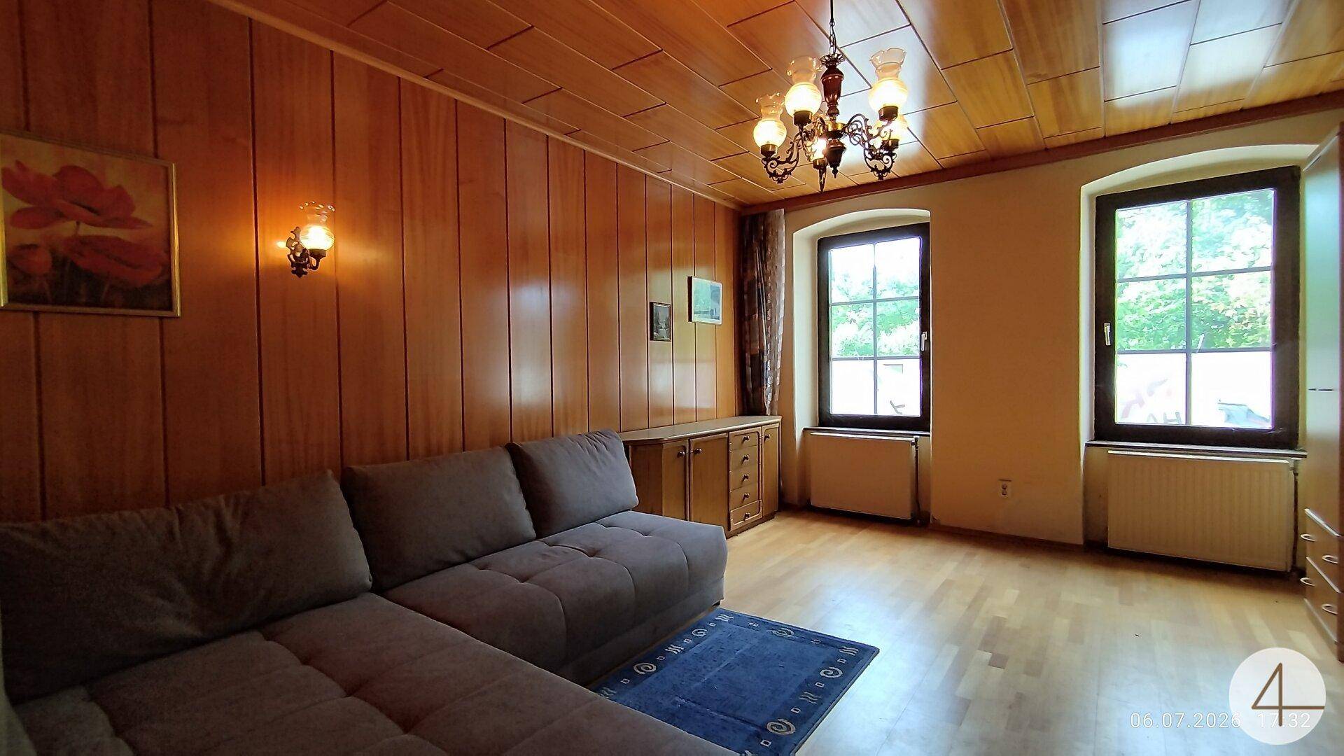 Gemütliches Wohnzimmer mit Holztäfelung, Parkettboden und traditioneller Deckenlampe.