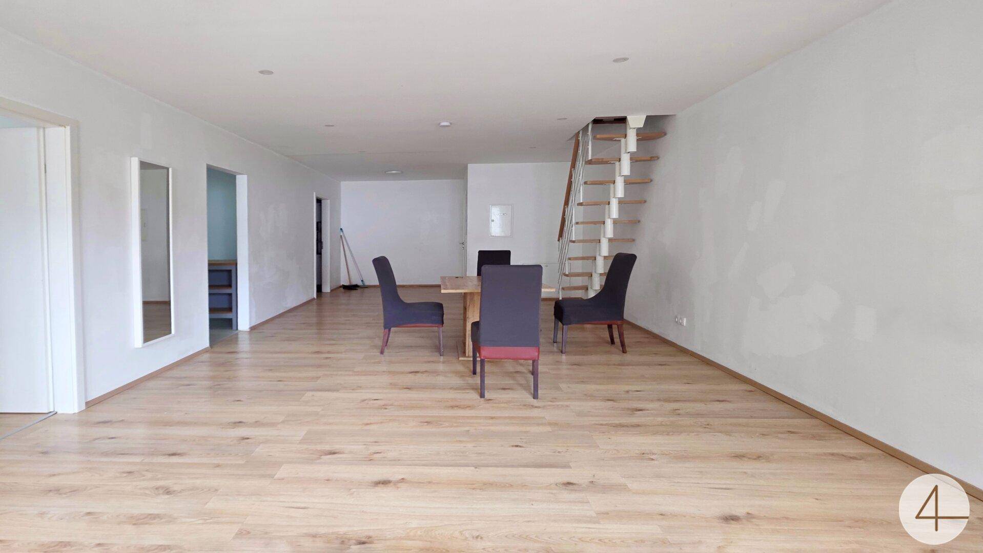 Geräumiger offener Wohn- und Essbereich mit hellem Holzboden und einer modernen Treppe.