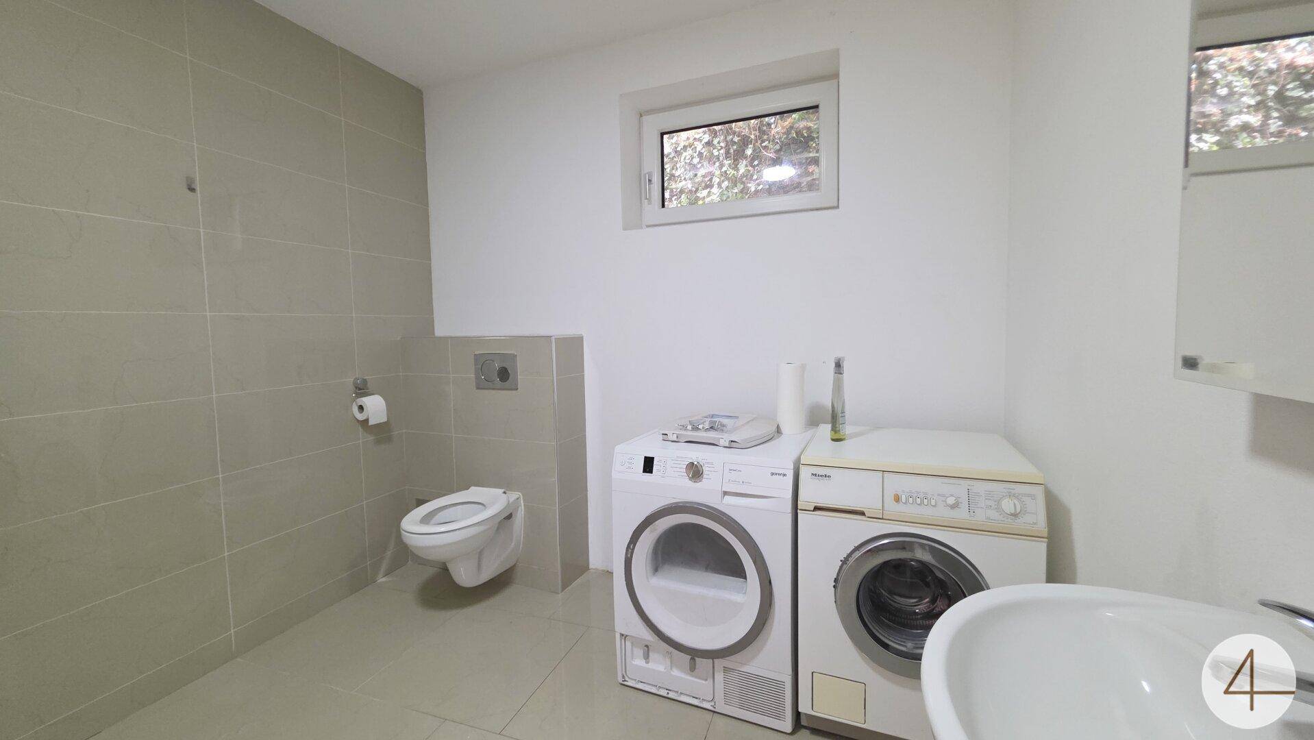 Modernes WC mit Wand-WC, Waschmaschine, Trockner und einem Fenster für Tageslicht.