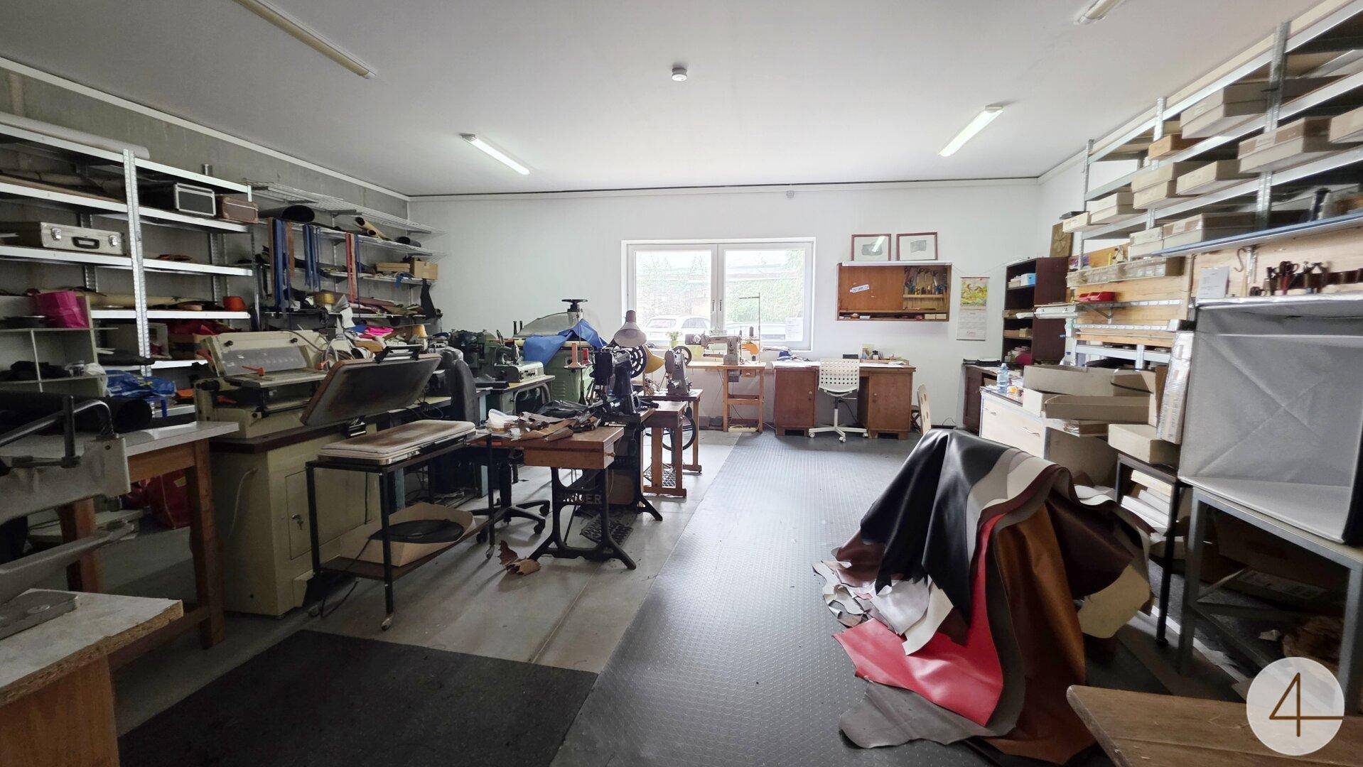 Großer Werkstattraum mit vielen Regalen, Arbeitsgeräten und einem Fenster.
