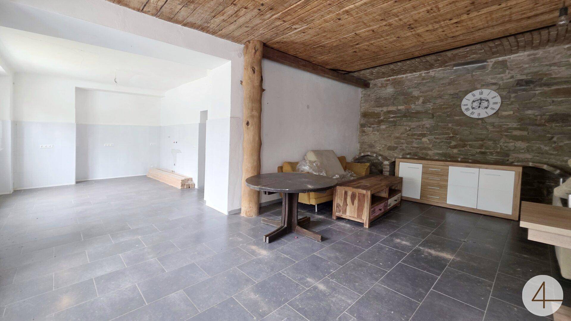 Rustikaler Wohnbereich mit Steinwand, Holzbalkendecke und dunklem Fliesenboden.