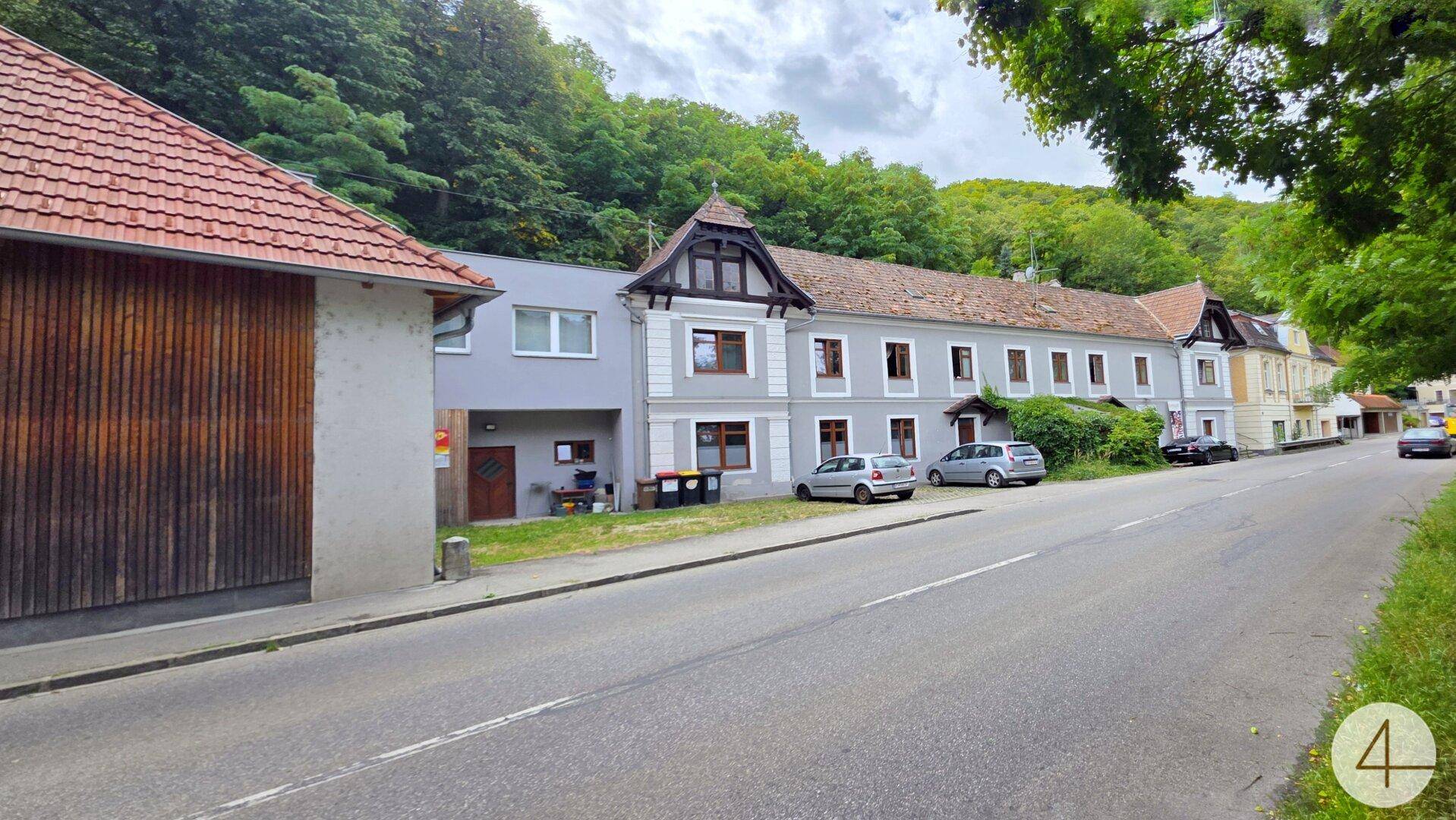 Reihe von Gebäuden entlang einer Straße, umgeben von üppiger grüner Vegetation und Bäumen.