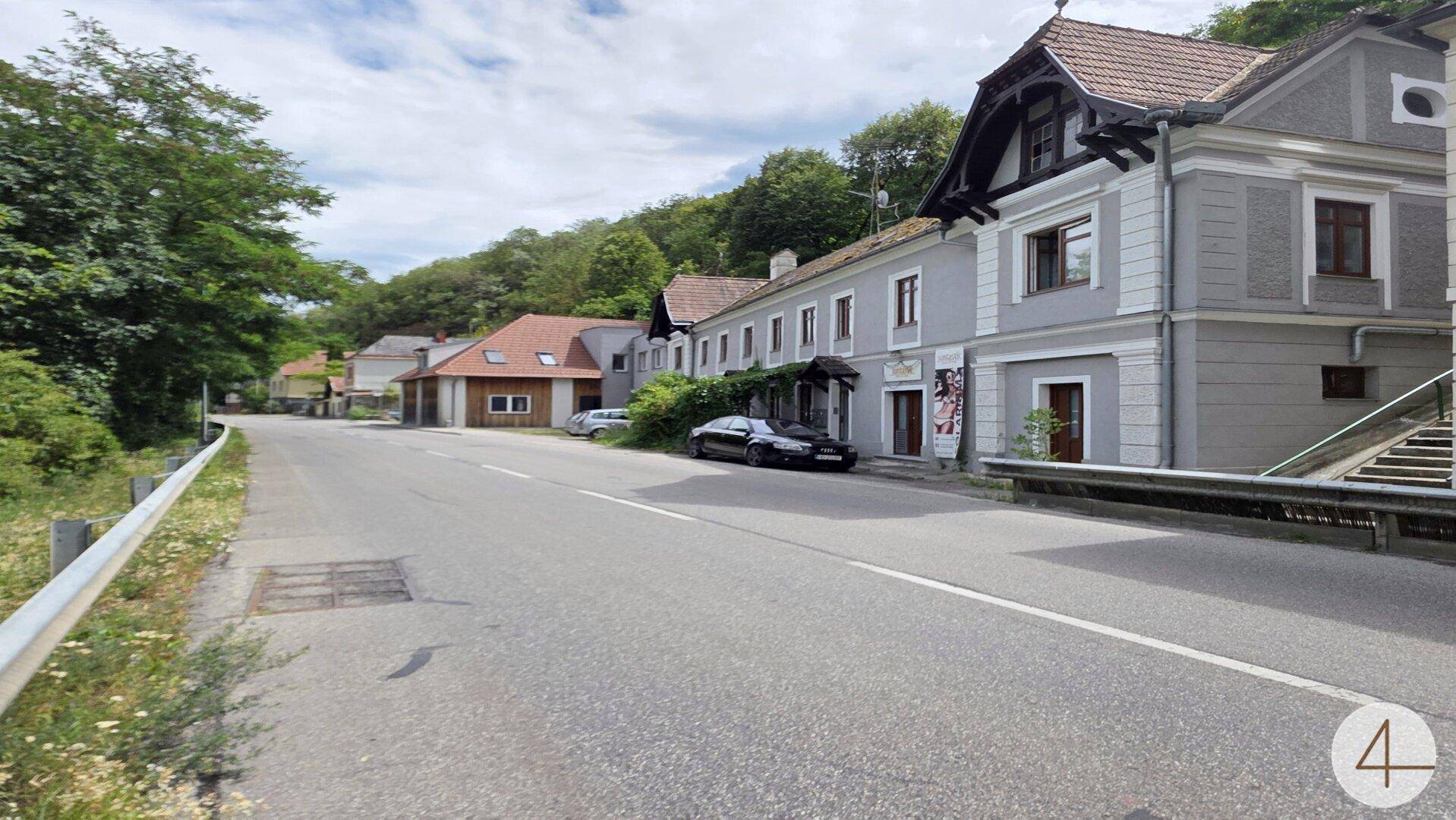 Straße mit einer Reihe von Gebäuden, darunter ein modernes Holzhaus und ältere Häuser.