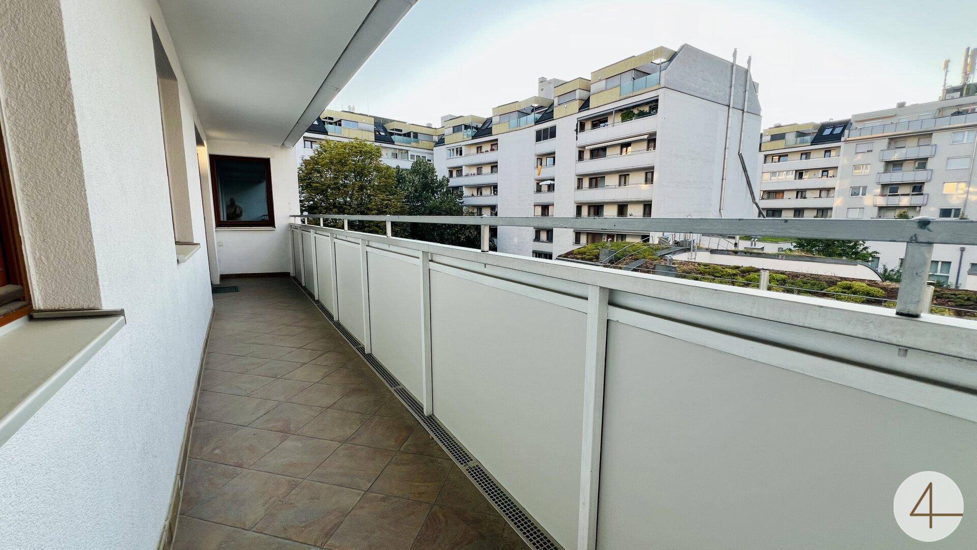 Geräumiger Balkon mit Fliesenboden und Ausblick auf die umliegende Wohnbebauung und Bäume.