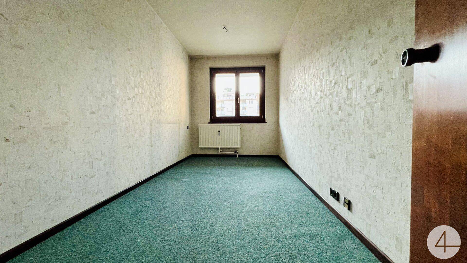Leerer Raum mit grüner Teppichboden und Fenster, bereit für eine individuelle Gestaltung.