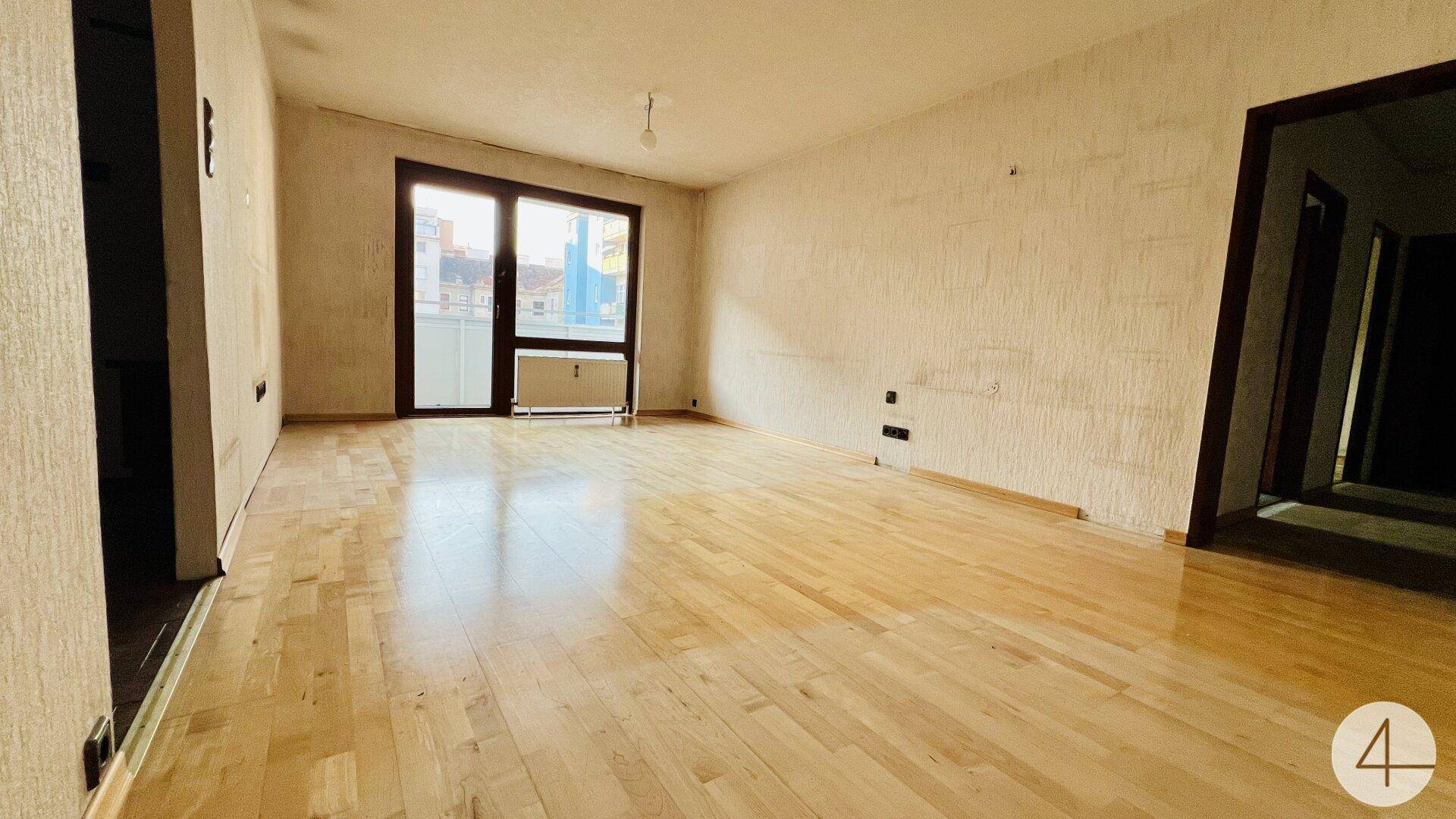 Heller Wohnraum mit Holzdielenboden und großem Fenster, das Zugang zum Balkon bietet.