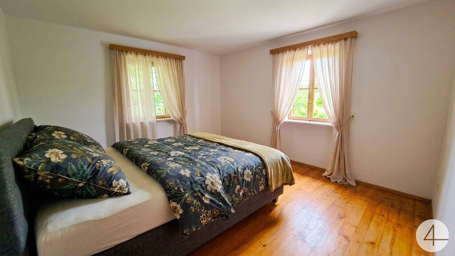 Helles Schlafzimmer mit Holzboden, zwei Fenstern und einem gemütlichen Doppelbett.