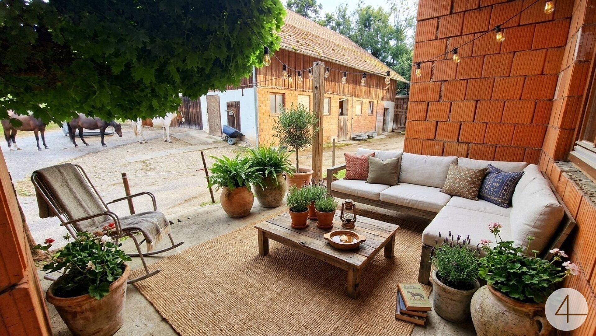 Rustikale Terrasse mit bequemen Gartenmöbeln und Blick auf den Hof mit Pferden.