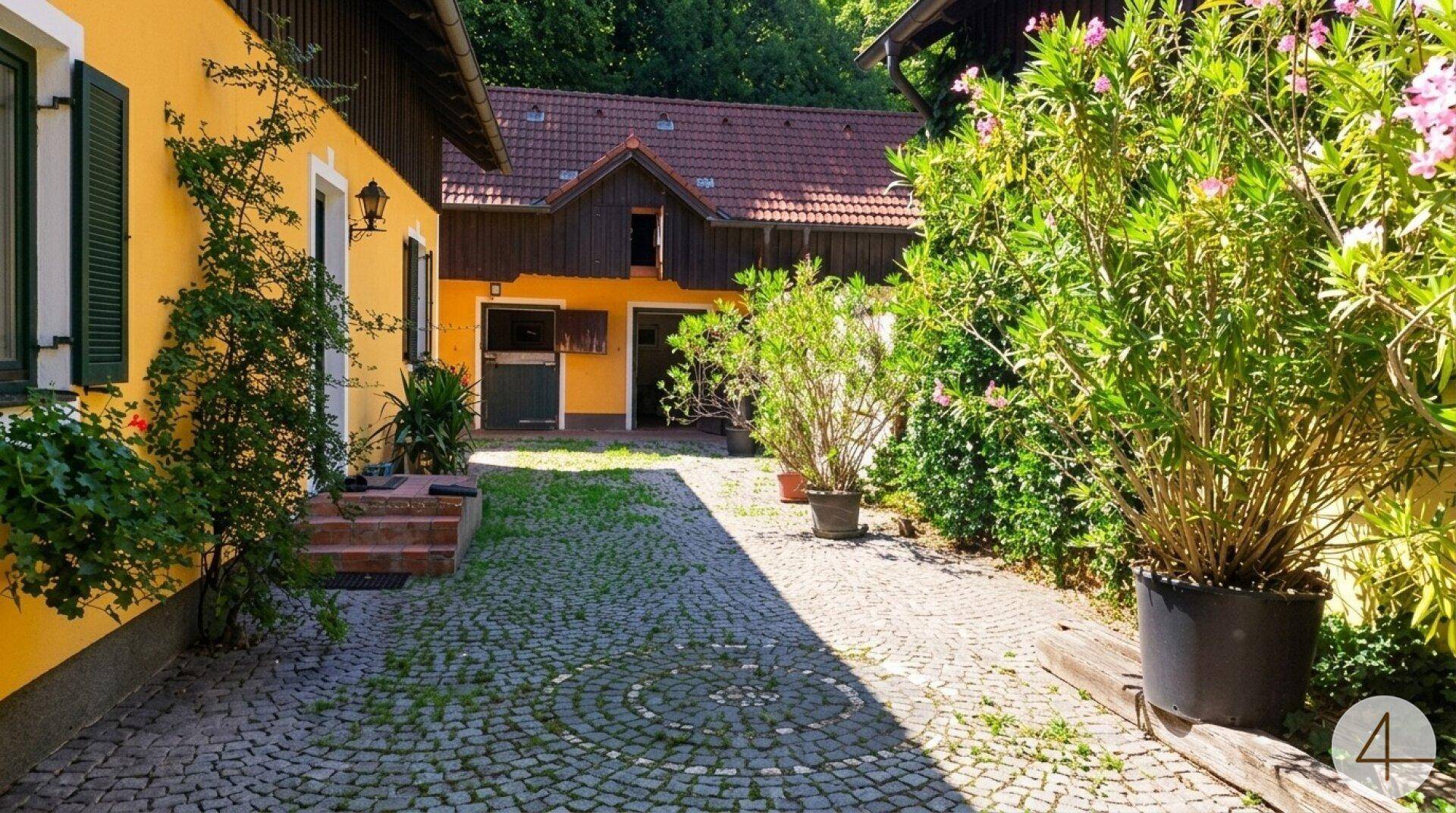 Idyllischer Innenhof mit Kopfsteinpflasterweg, umgeben von gelb gestrichenen Gebäuden und üppiger Bepflanzung.
