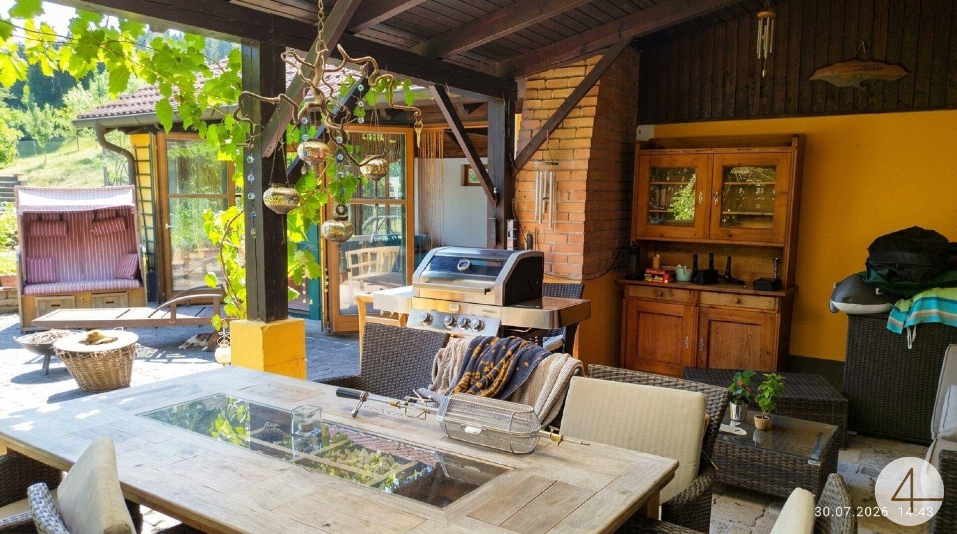 Gemütlicher überdachter Terrassenbereich mit großem Esstisch, Grill und rustikalen Möbeln für gesellige Stunden.
