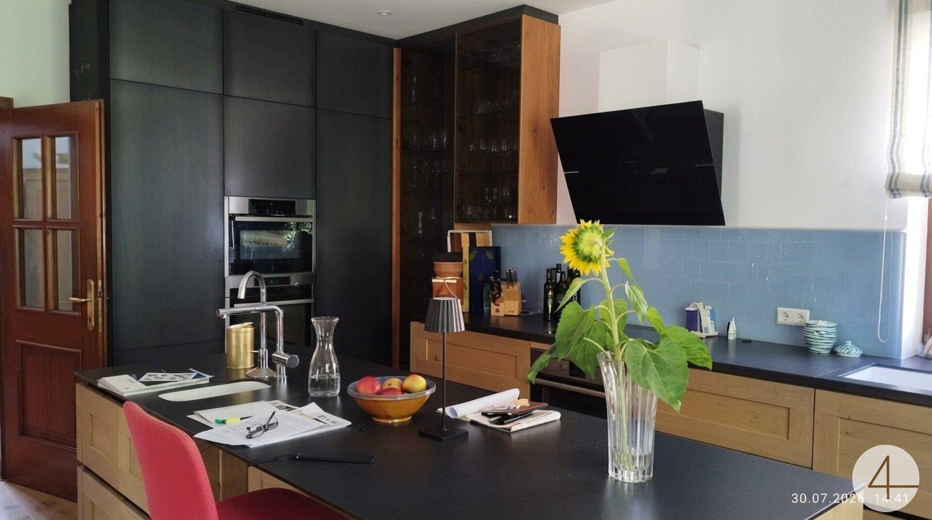 Moderne Küche mit schwarzer Arbeitsplatte, Holzfronten und Kücheninsel, ausgestattet mit hochwertigen Geräten.