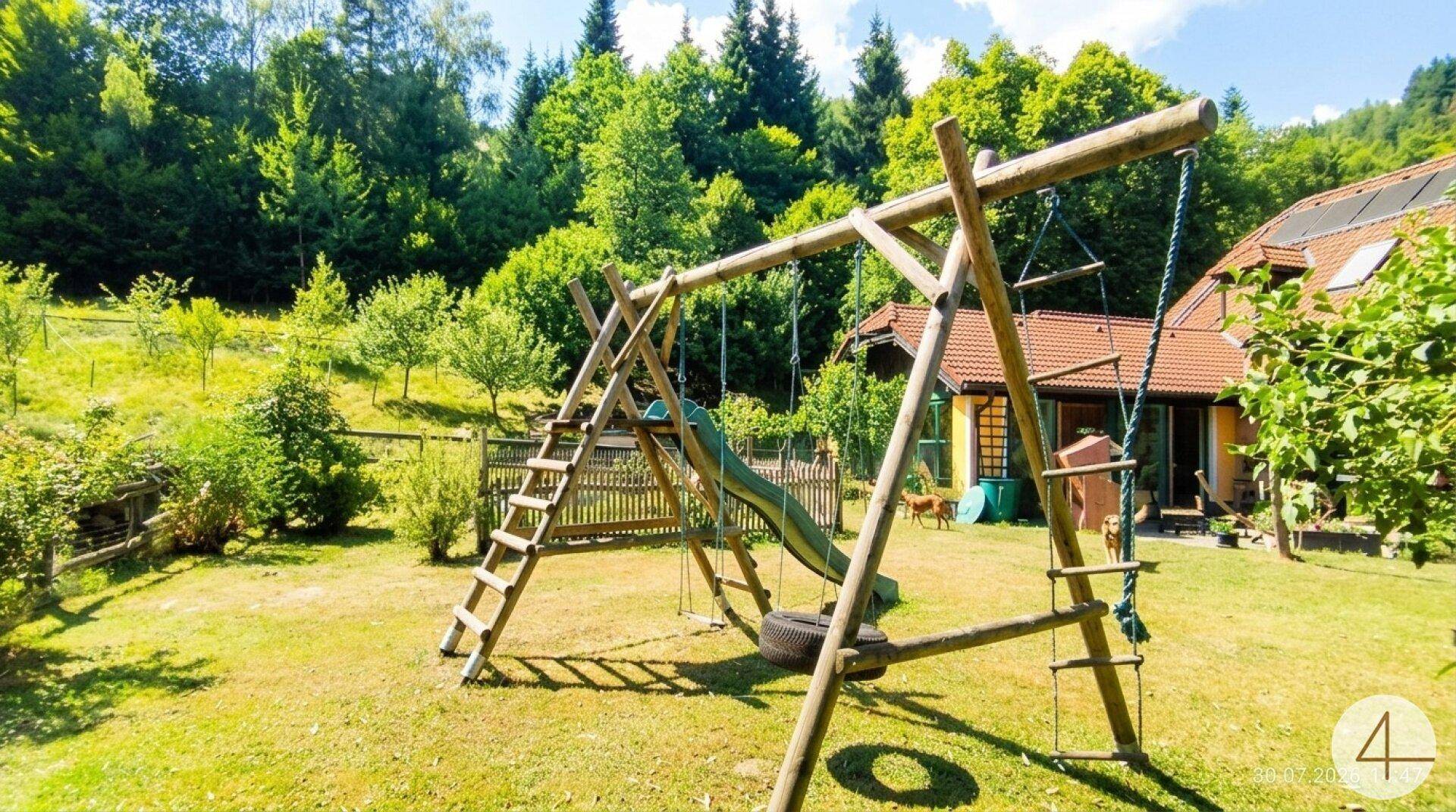 Kinderspielplatz mit Schaukelgerüst und Rutsche auf einer weitläufigen Rasenfläche vor dem Haus.