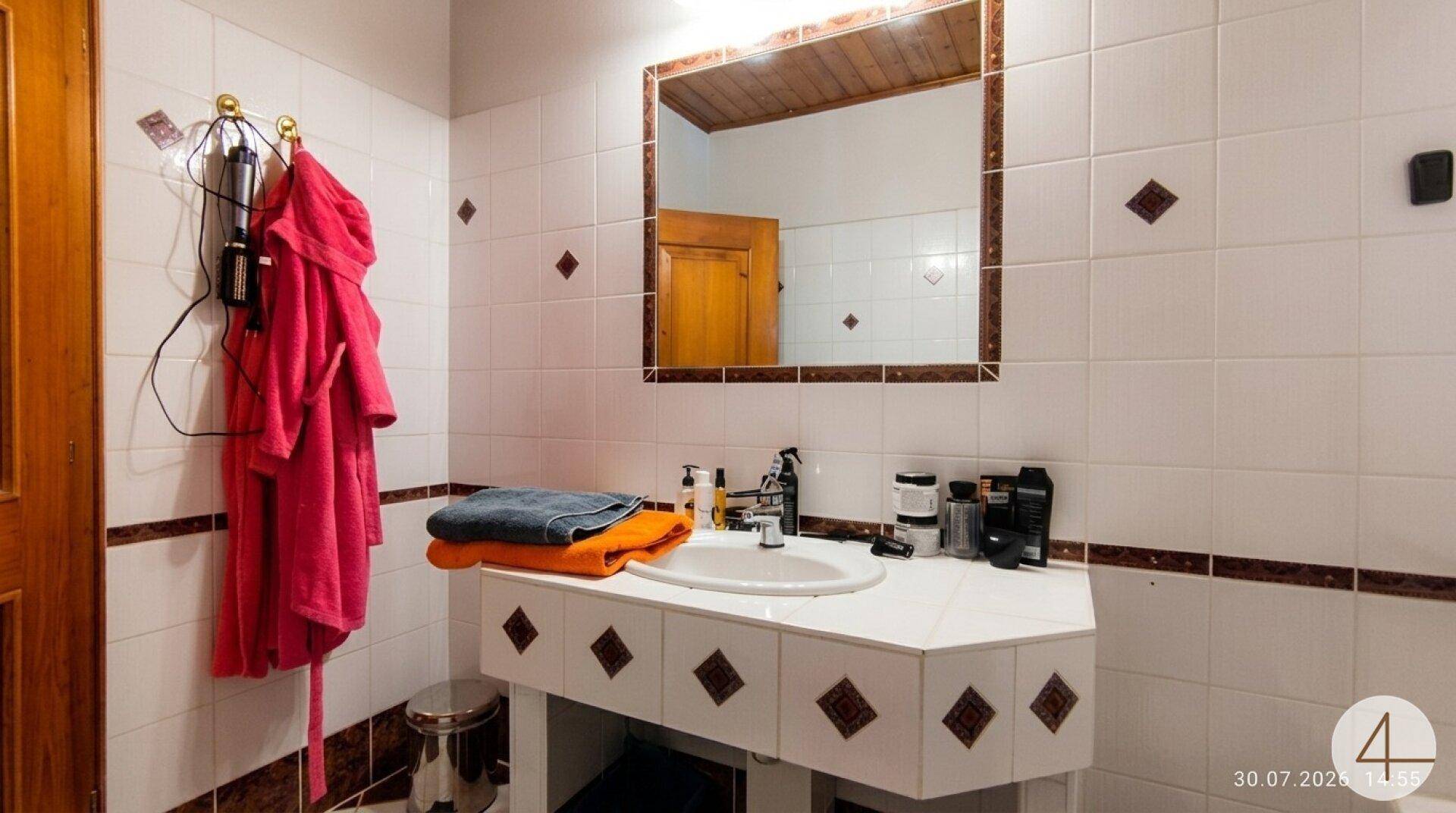 Traditionelles Badezimmer mit weißen Fliesen, Einzelwaschbecken und Holzspiegelrahmen.