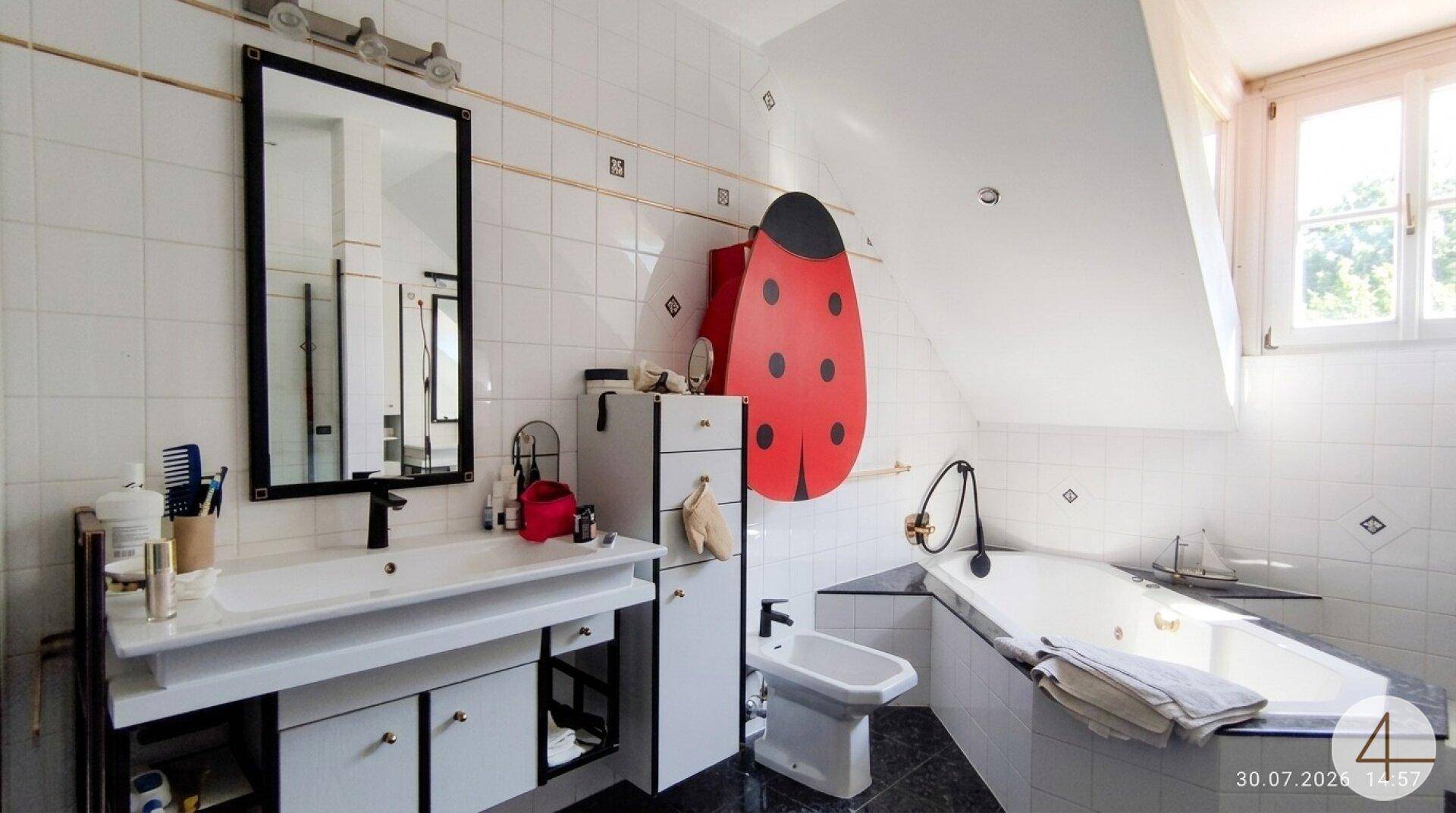 Helles Badezimmer im Dachgeschoss mit Badewanne, Bidet und Fenster, dekoriert mit einer Marienkäferfigur.