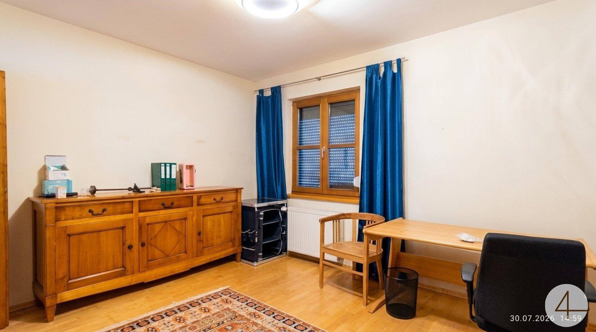 Helles Arbeitszimmer mit Holzmöbeln, Teppich und Fenster, ideal als Büro oder Gästezimmer nutzbar.