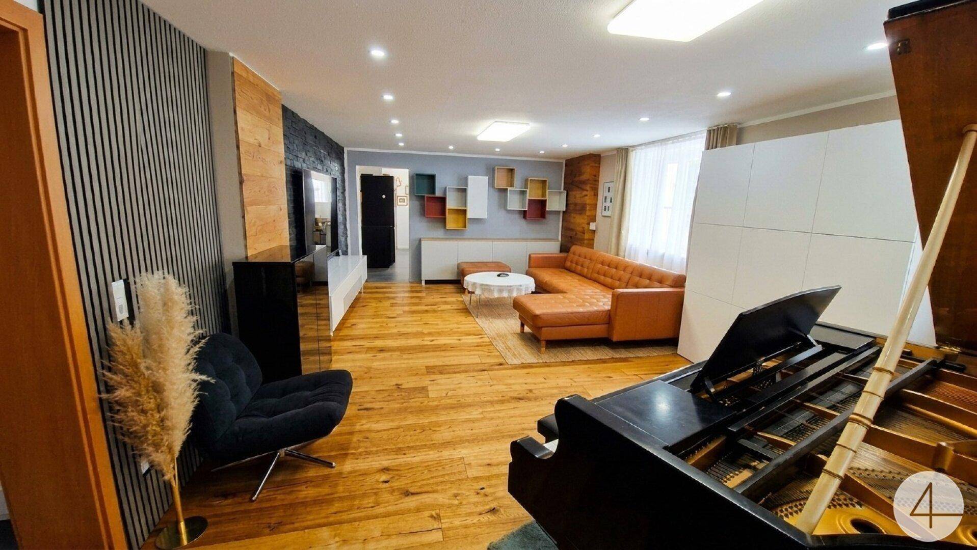 Geräumiges Wohnzimmer mit Flügel, Ledersofa, Holzboden und modernen Wandverkleidungen.