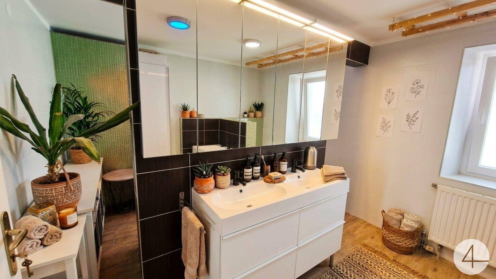 Helles Badezimmer mit Doppelwaschbecken, großem Spiegelschrank und Fenster.