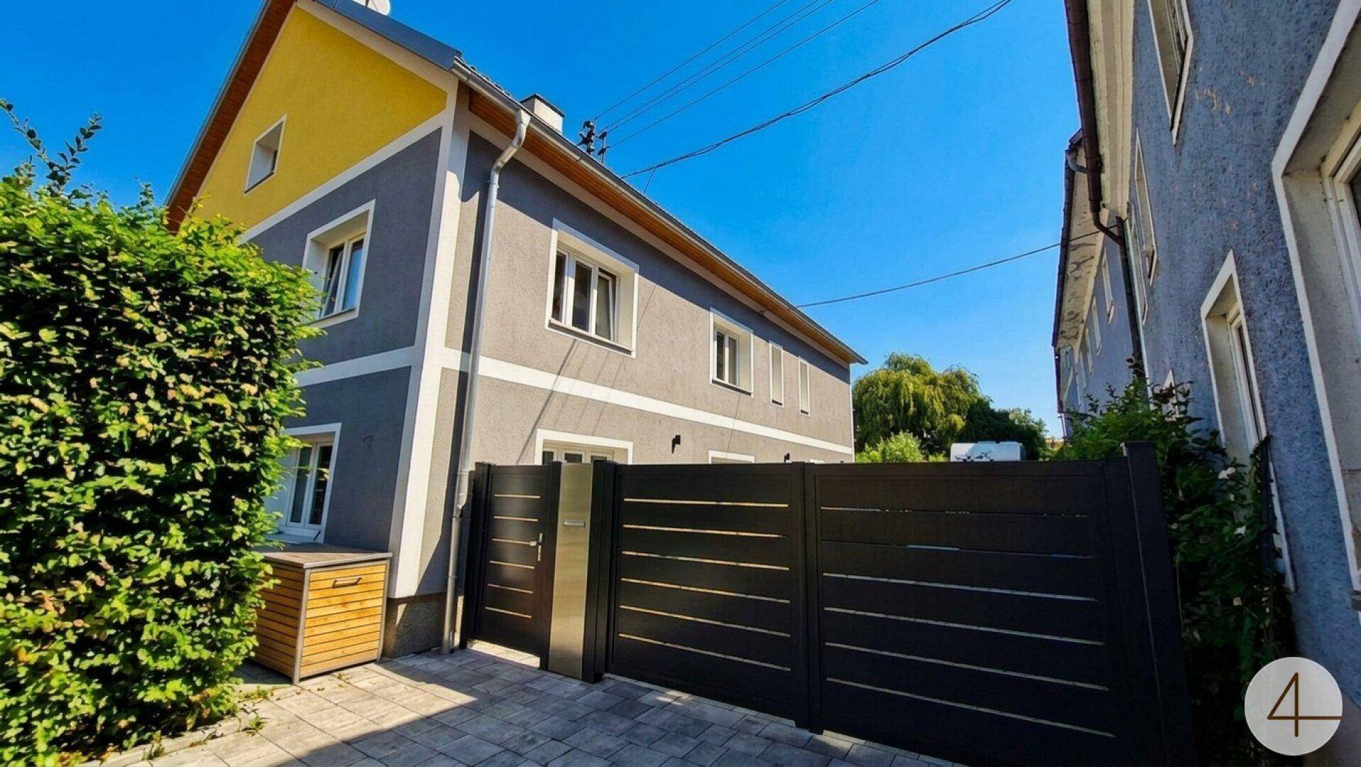 Moderne Hausfassade in Grau und Gelb mit stilvollem schwarzen Zaun.