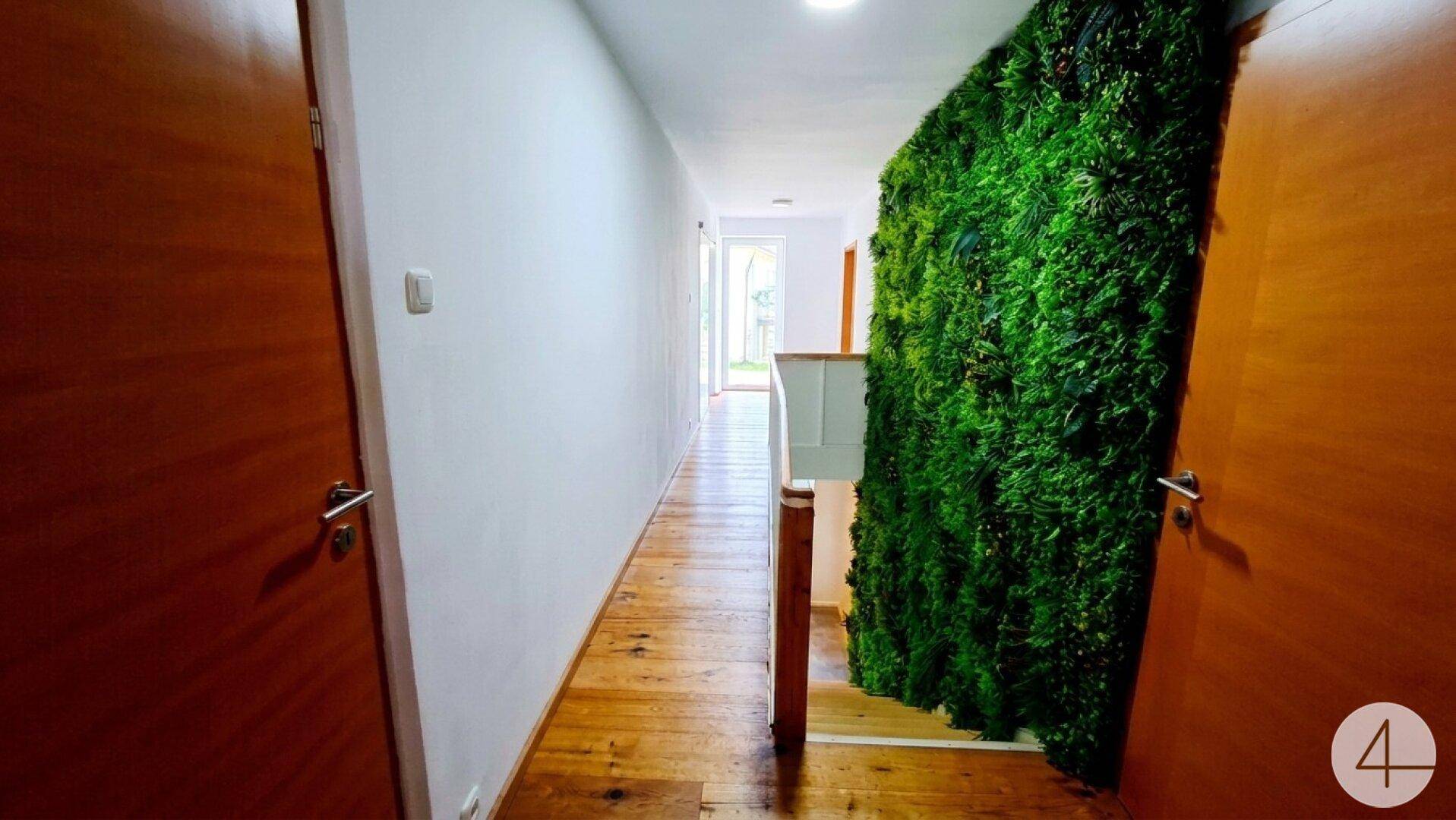 Heller Flur mit Holzboden und einer auffälligen grünen Mooswand als Dekoration.
