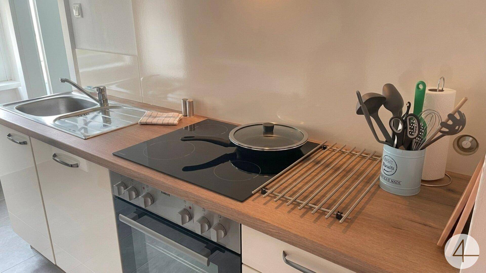 Detailansicht der Küchenzeile mit Spülbecken, Induktionskochfeld und Backofen, bereit zum Kochen.