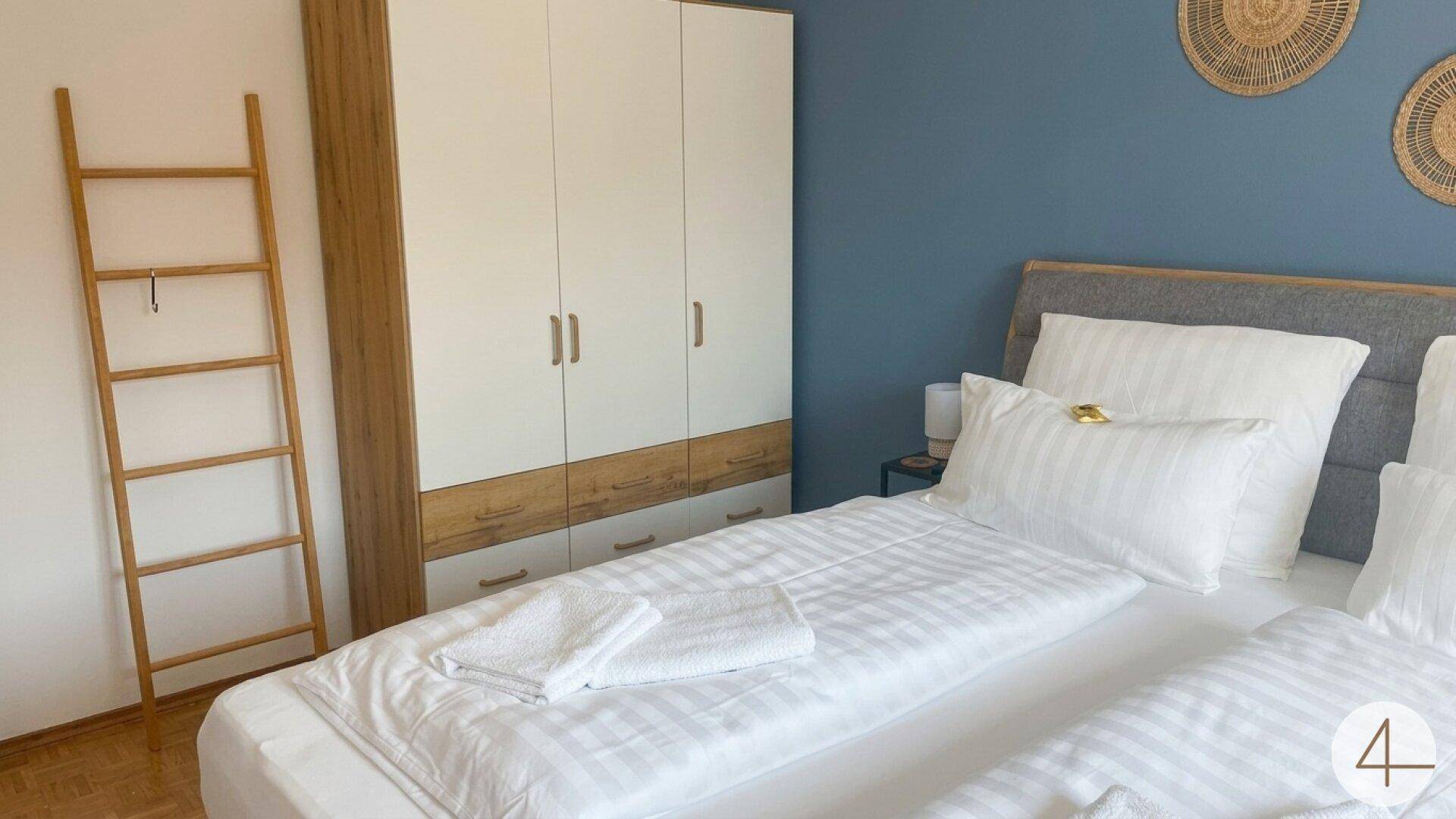 Schlafzimmer mit Doppelbett, blauer Wand und einem modernen Kleiderschrank mit Holzdetails.