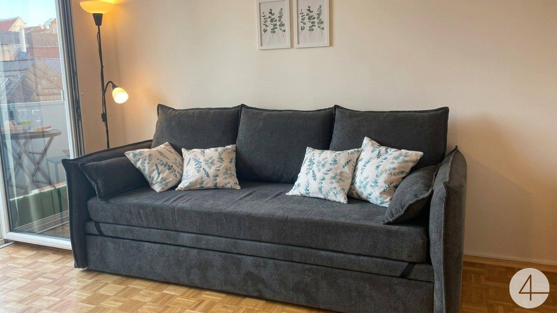 Bequemes Schlafsofa im Wohnzimmer mit dekorativen Kissen und Zugang zum sonnigen Balkon.
