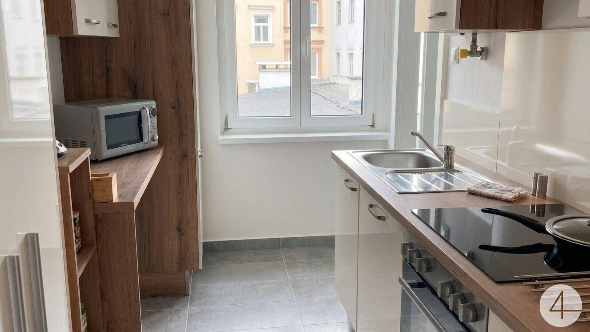 Funktionale Küchenzeile mit Spüle, Kochfeld, Backofen und Mikrowelle, ideal für kleine Mahlzeiten.
