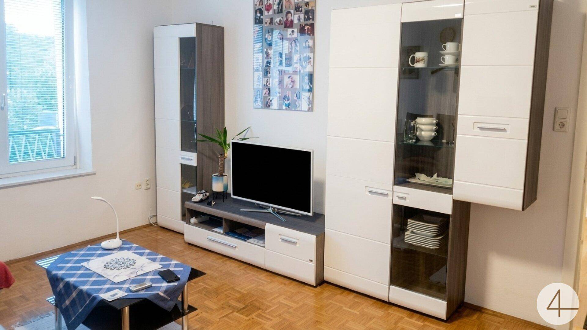 Helles Wohnzimmer mit Parkettboden, TV-Möbeln und Blick ins Grüne durch das Fenster.