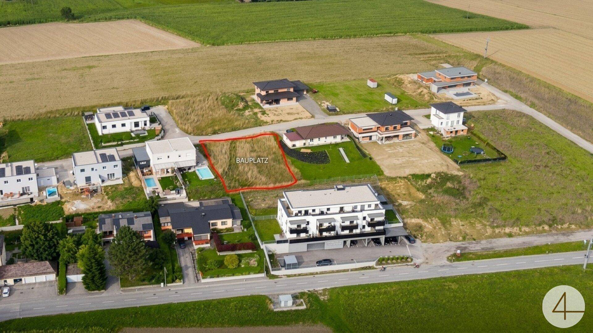 Luftaufnahme eines markierten Grundstücks in ländlicher Umgebung mit umliegenden Neubauten und Feldern.