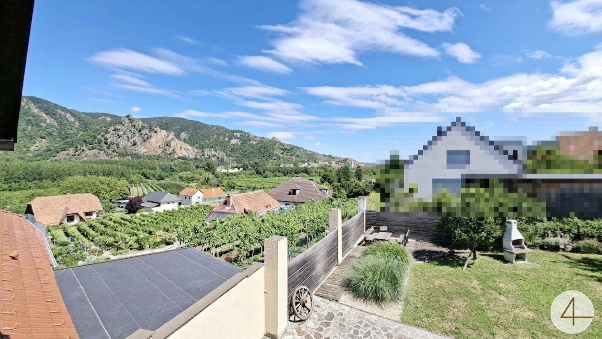 Panoramablick auf die umliegende Landschaft mit Weinbergen, Bergen und einem Garten mit Grillplatz.