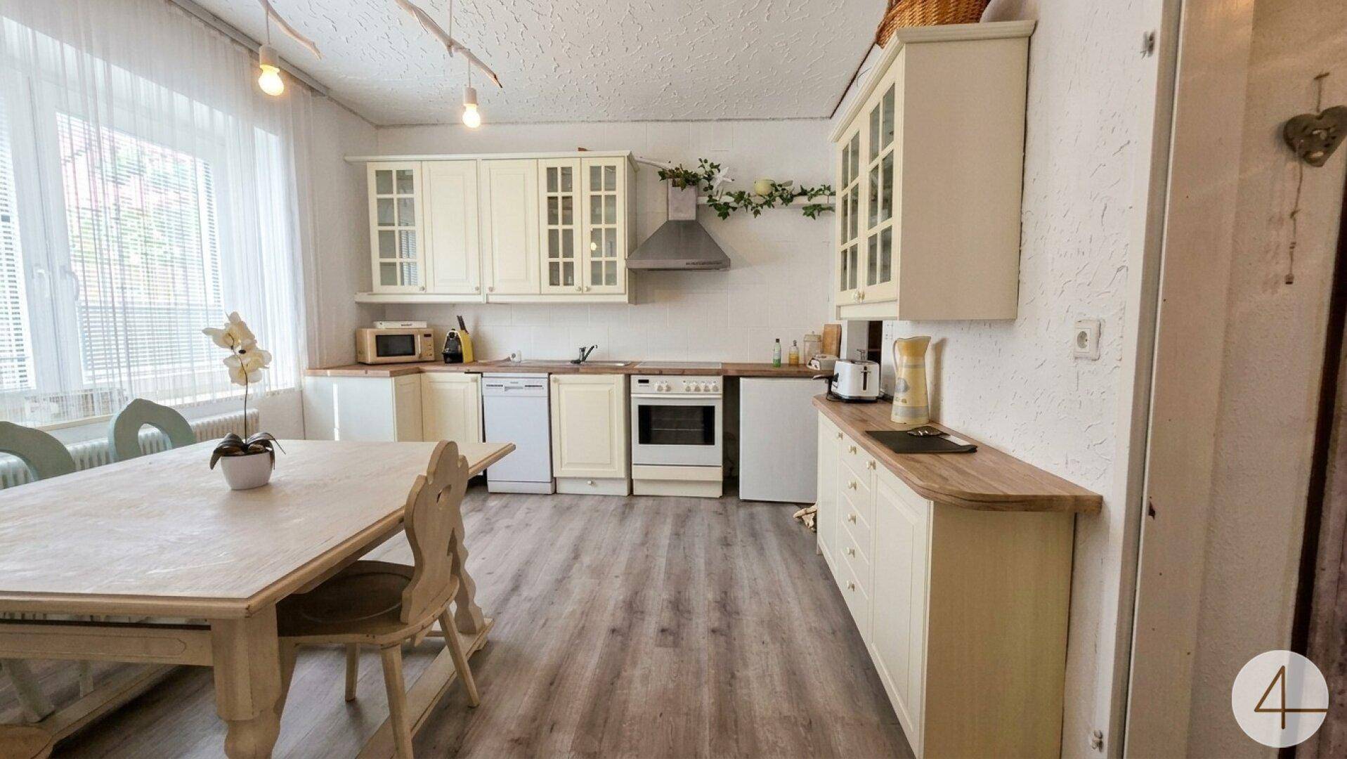 Helle Einbauküche mit Essbereich, cremefarbenen Schränken, Holzarbeitsplatte und modernen Geräten.
