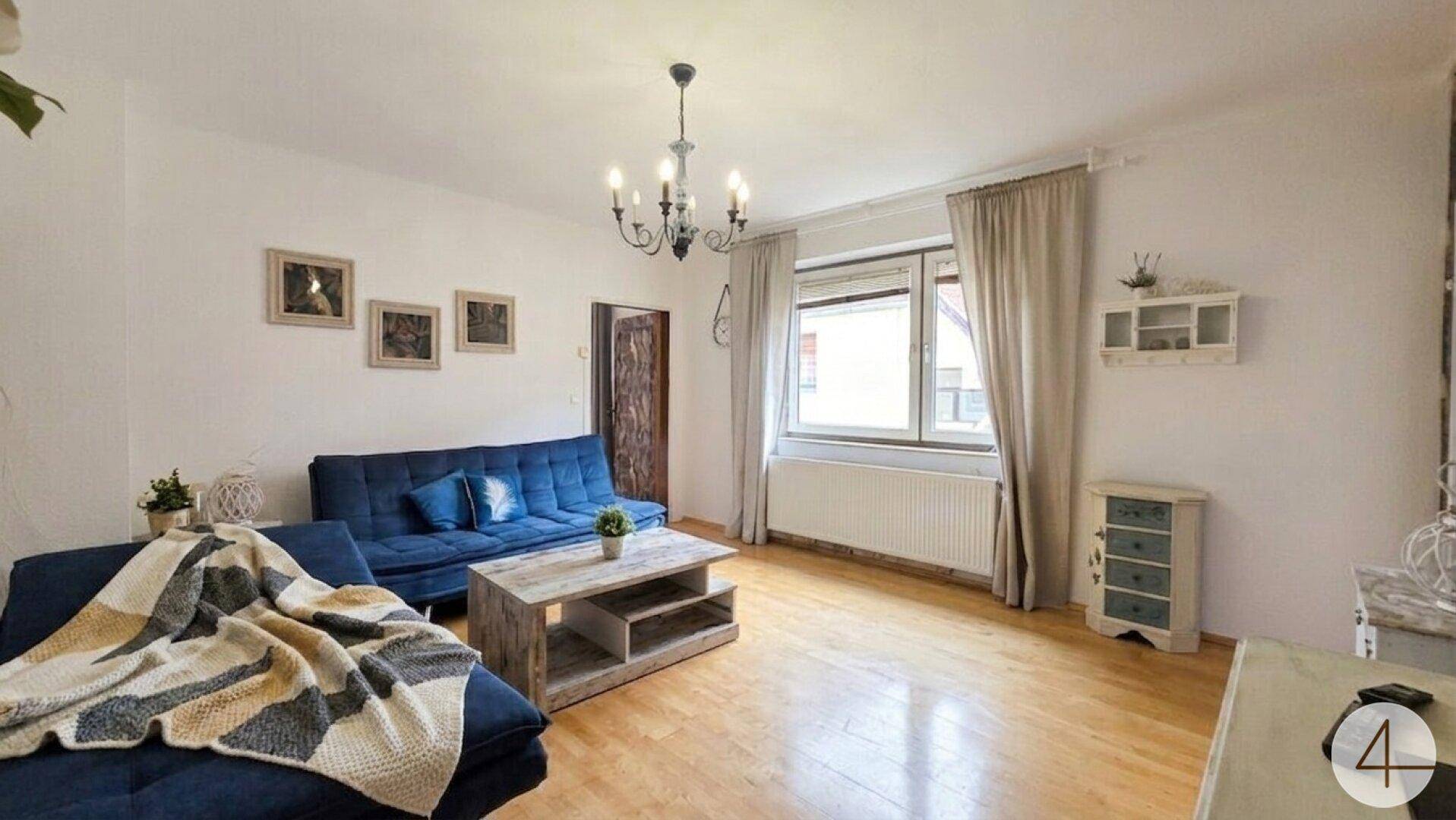 Wohnzimmer mit blauem Sofa, rustikalem Couchtisch und hellem Holzboden.