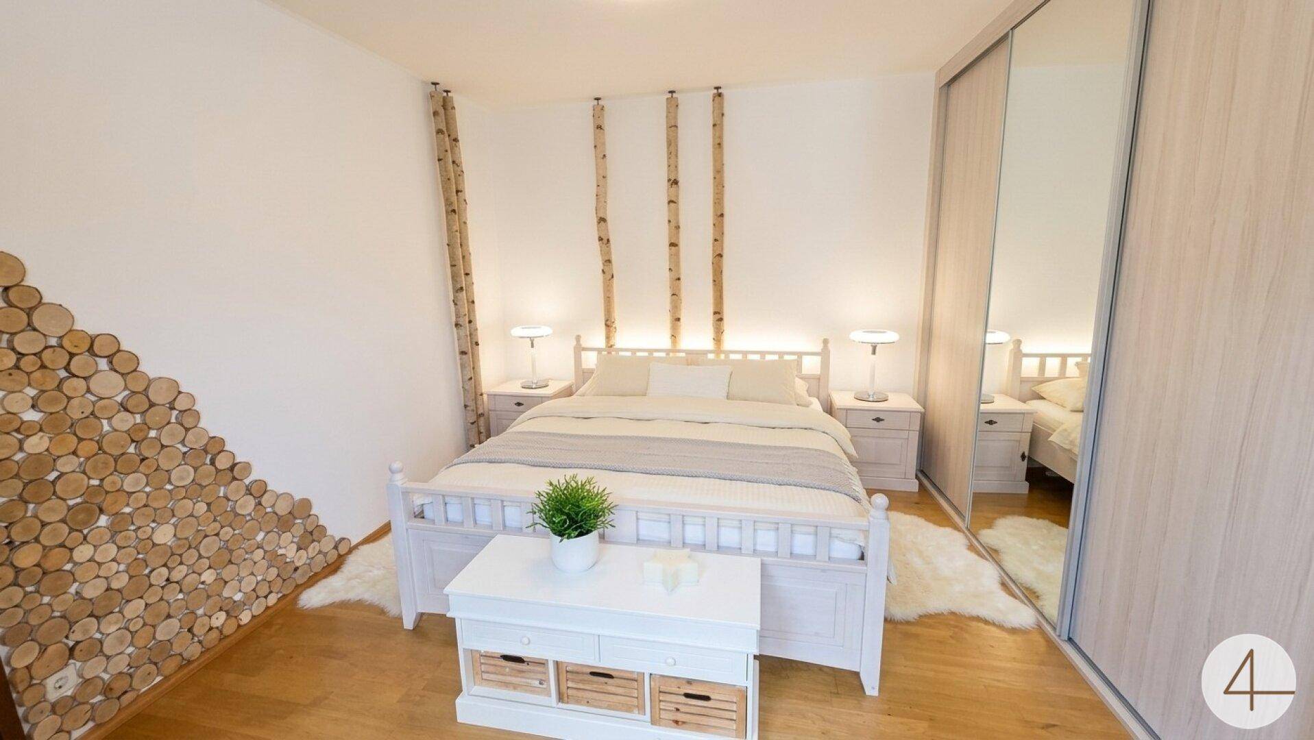 Gemütliches Schlafzimmer mit weißem Bett, dekorativen Holzelementen und Spiegelschiebetüren.