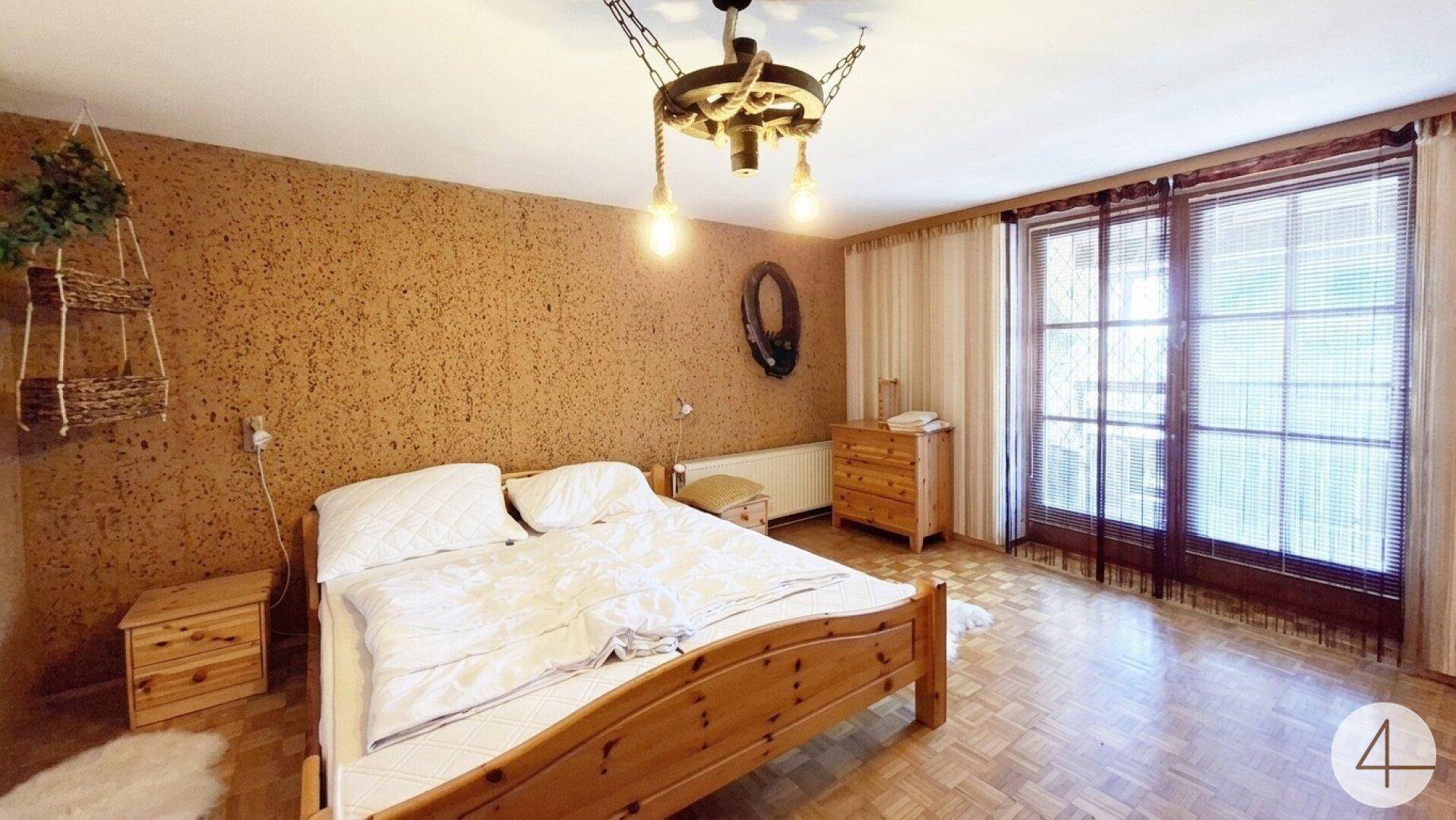 Schlafzimmer mit Doppelbett, Holzboden und Zugang zu einem Balkon oder einer Terrasse.