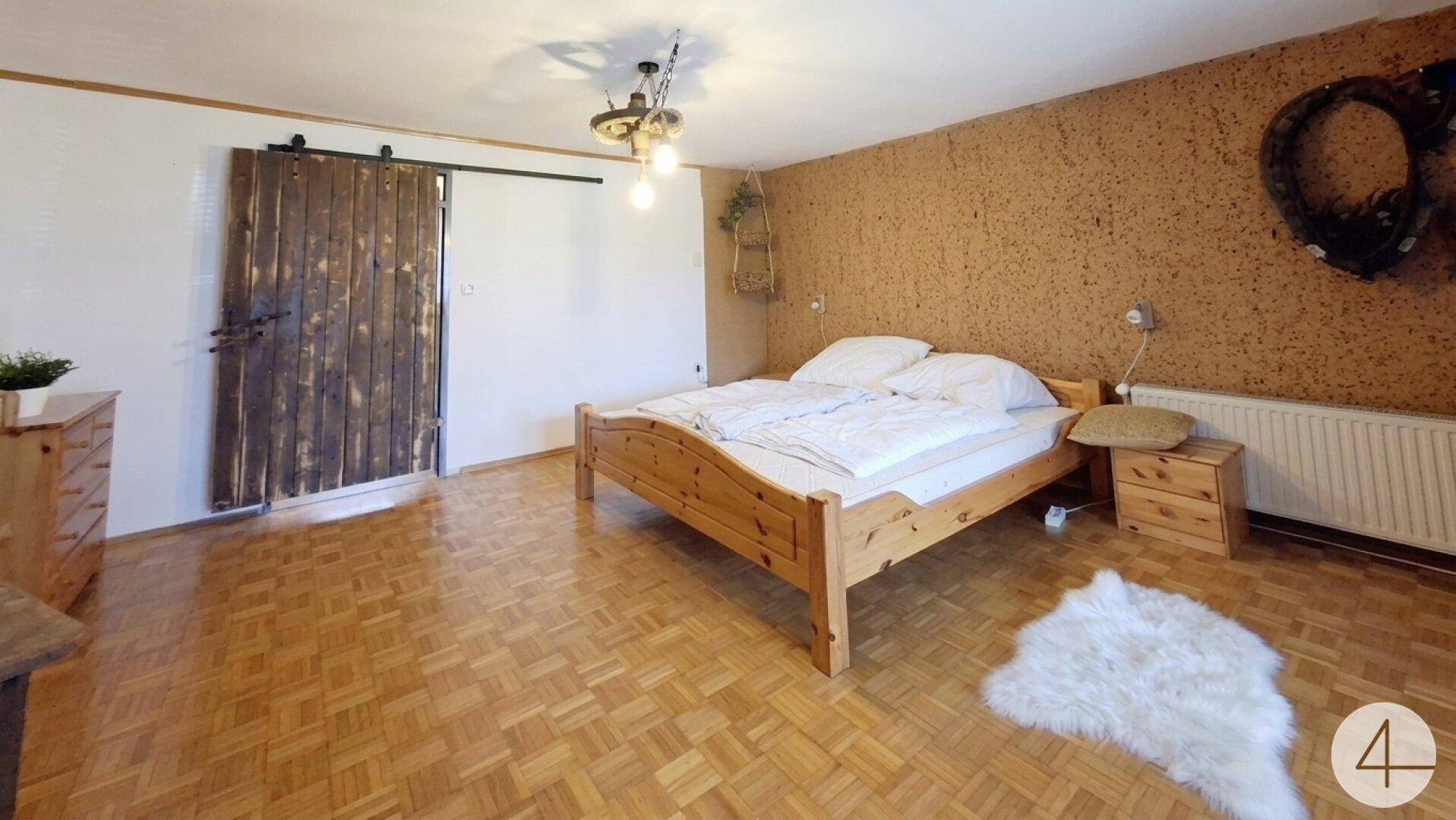 Geräumiges Schlafzimmer mit Holzboden, rustikaler Schiebetür und Korkwand.